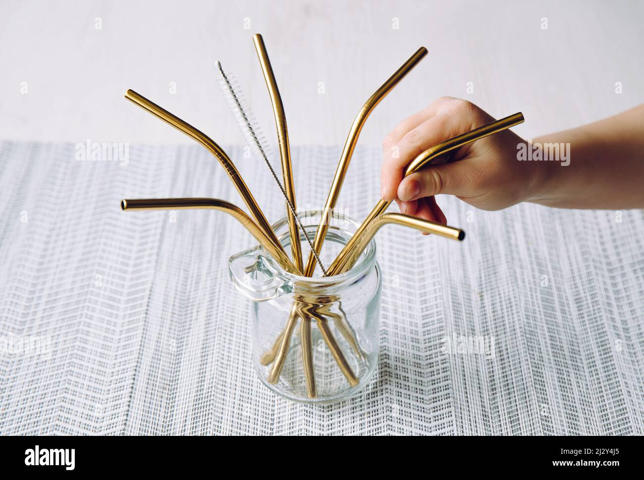 Child hand take golden metal drinking straw from glass jar in home kitchen. Sustainable lifestyle concept. Stock Photo