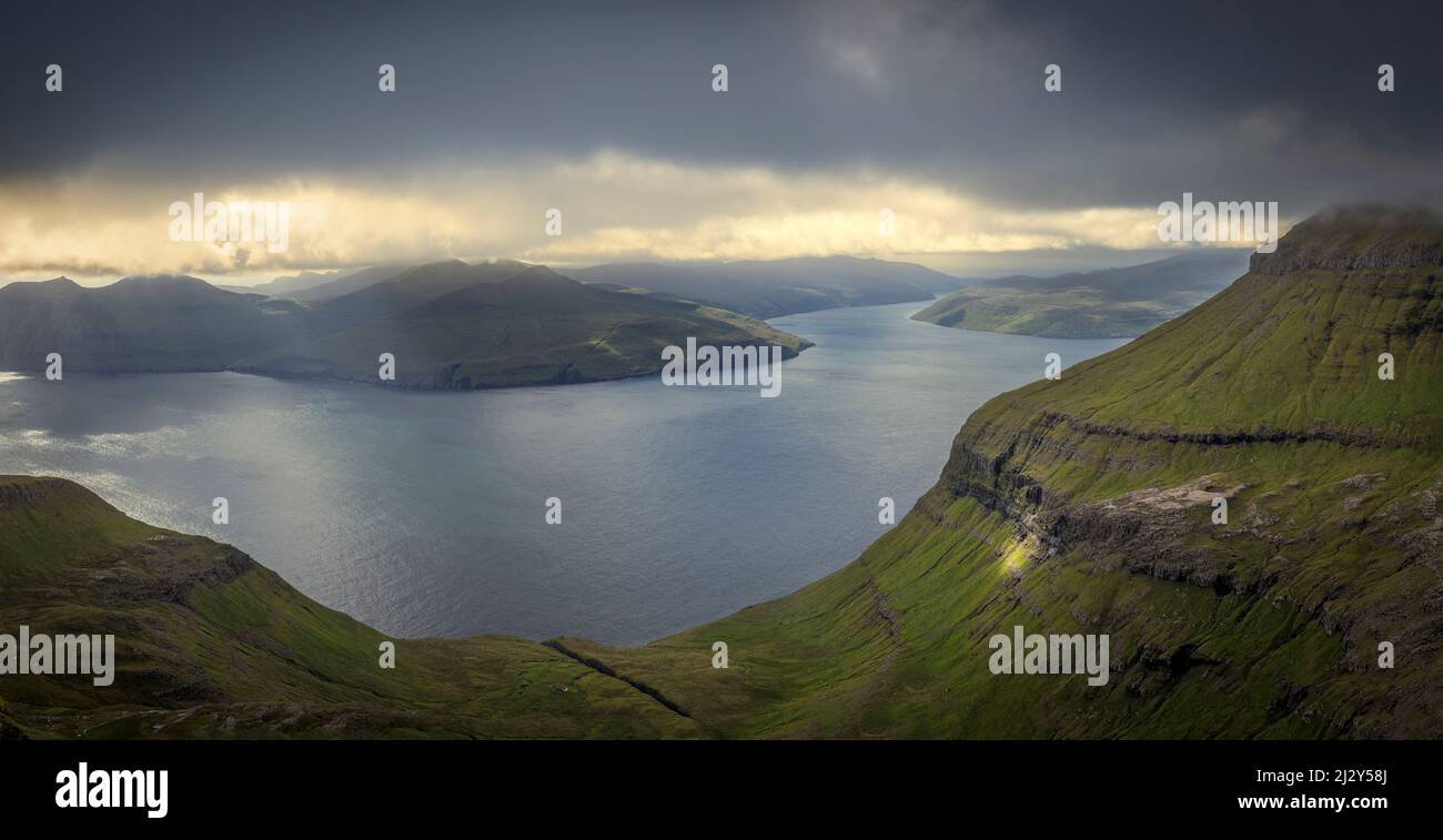View from Streymoy towards Eysturoy, Faeroer. Fjords, mountains, dark sky, cloud gap. Stock Photo