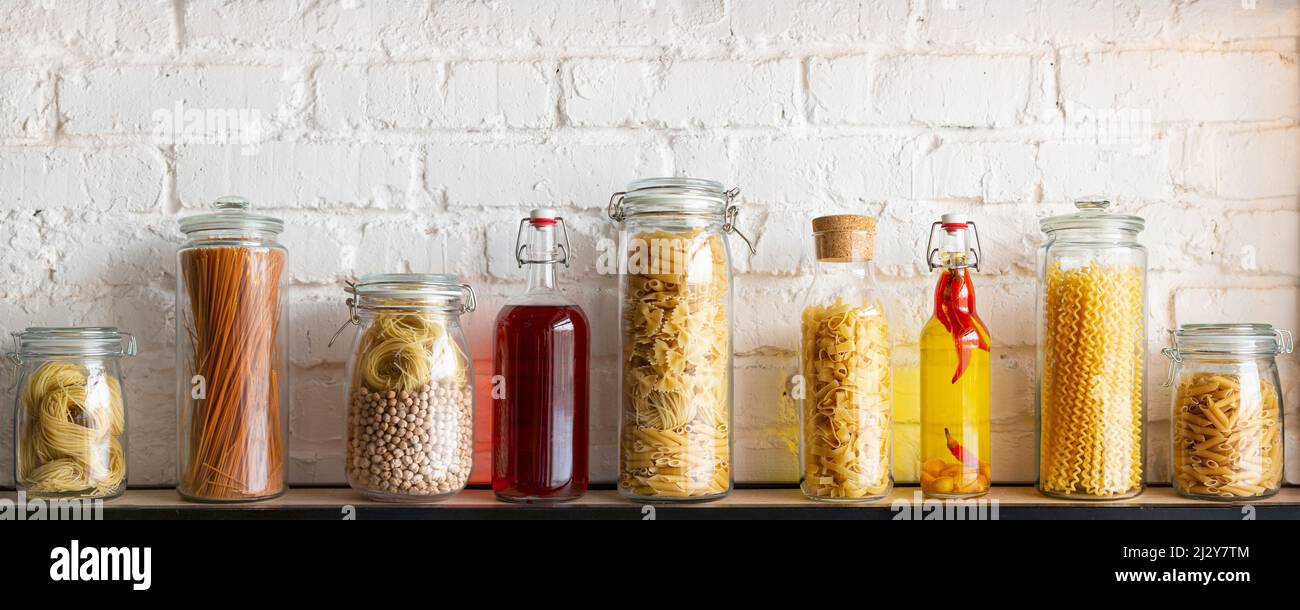 Kitchen shelf with jars of dry pasta, seasonings and sauces. Format photo 10x4. Stock Photo