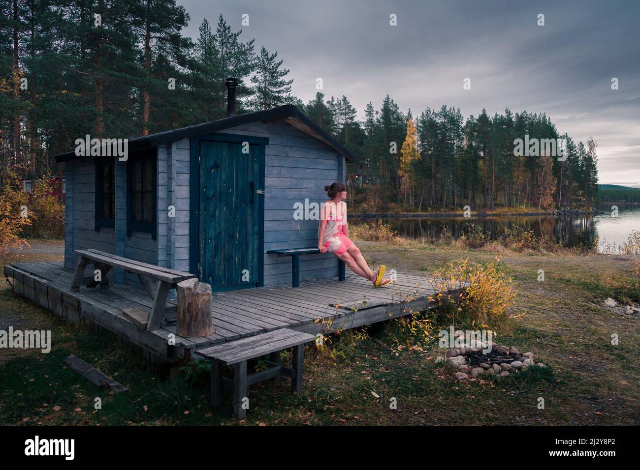 Woman sitting in front of sauna by the lake in Lapland, Sweden Stock Photo