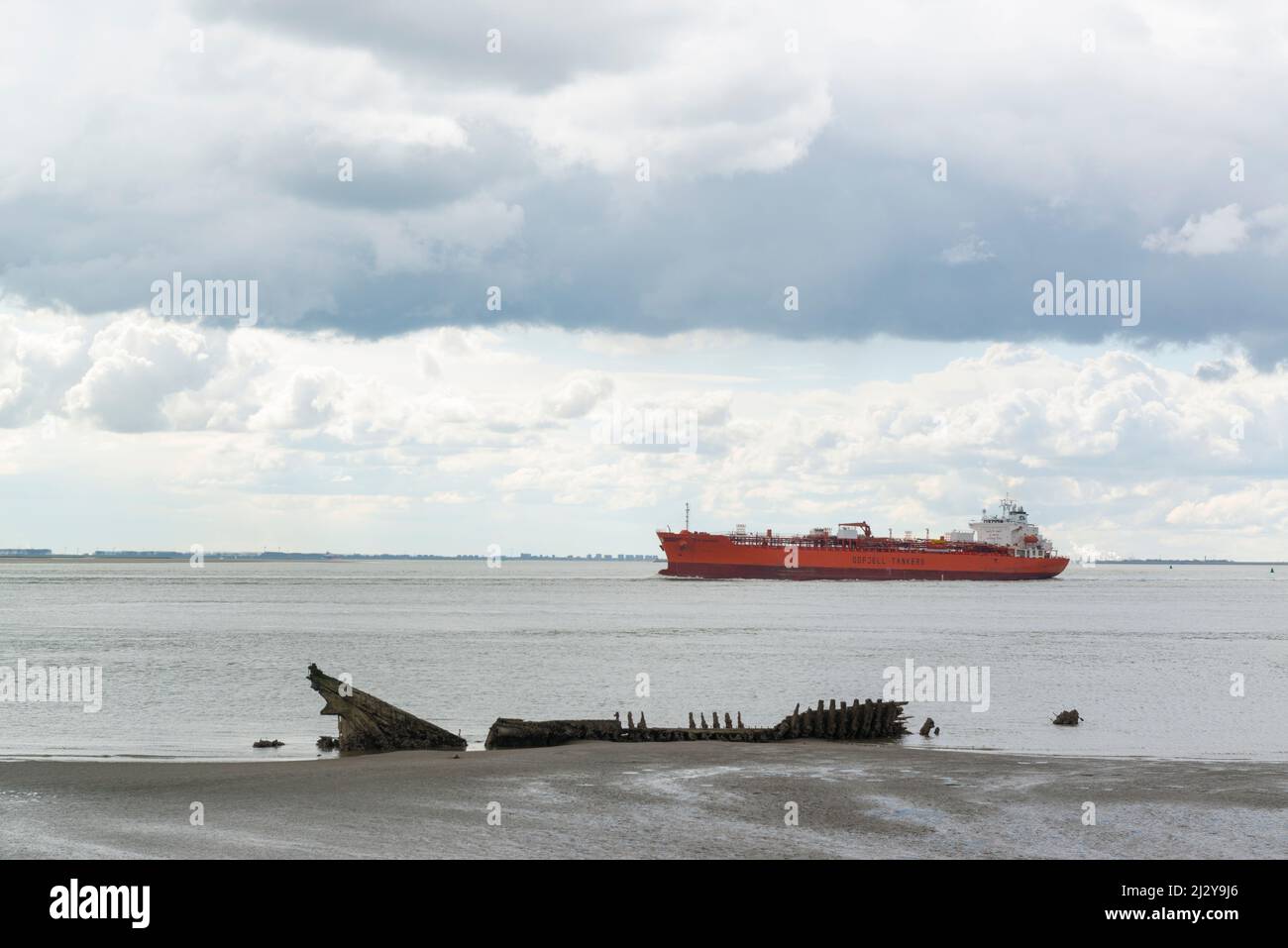 Tanker Bow Engineer of Odfjell Shipping on its way to Antwerp port passes a wooden ship wreck at the mudflats near Hansweert, Zeeland, Netherlands Stock Photo