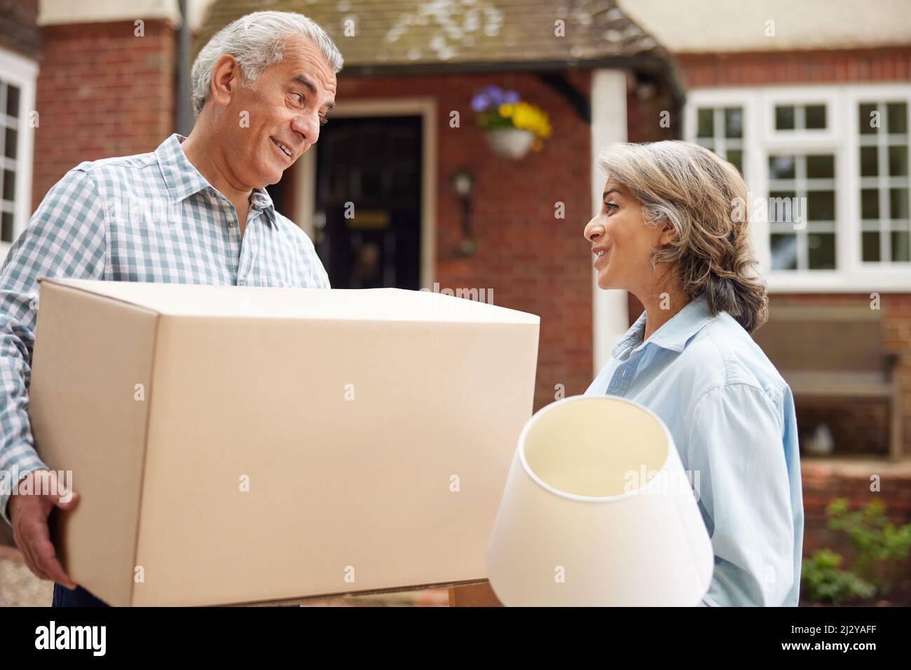 Mature Couple Carrying Boxes On Moving Day In Front Of Dream Home Stock Photo