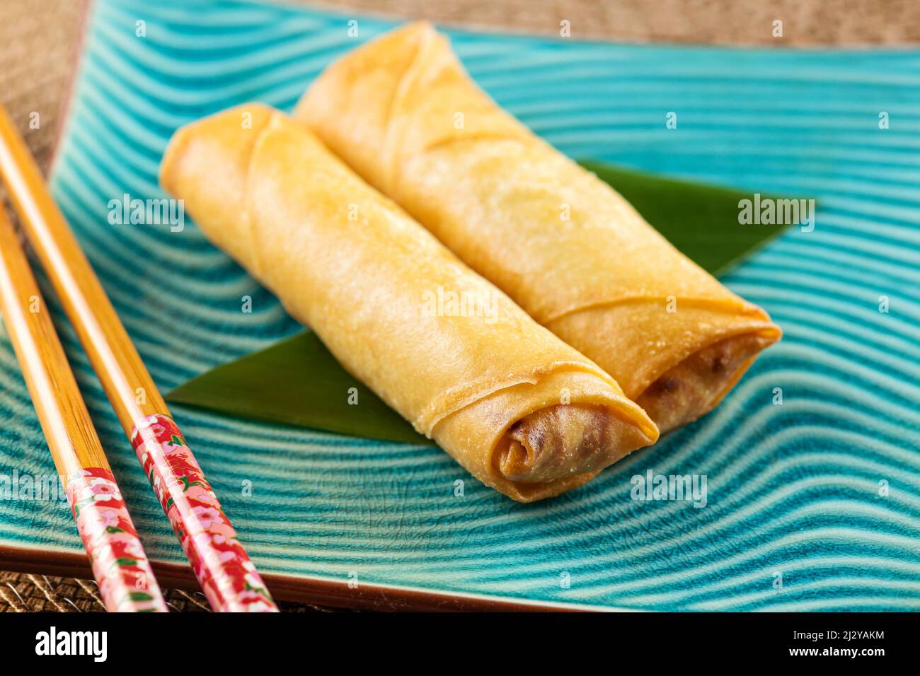 From above of delicious fresh spring rolls and wooden chopsticks placed on ceramic plate on table Stock Photo