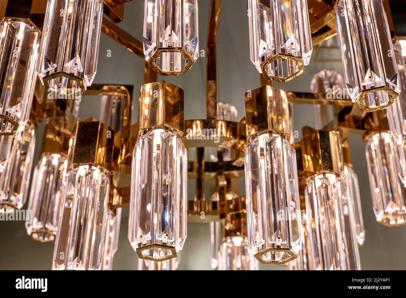 Close up on the stylish faceted glass prisms of a modern chandelier with gold or brass detail hanging from a ceiling in an interior decor concept Stock Photo