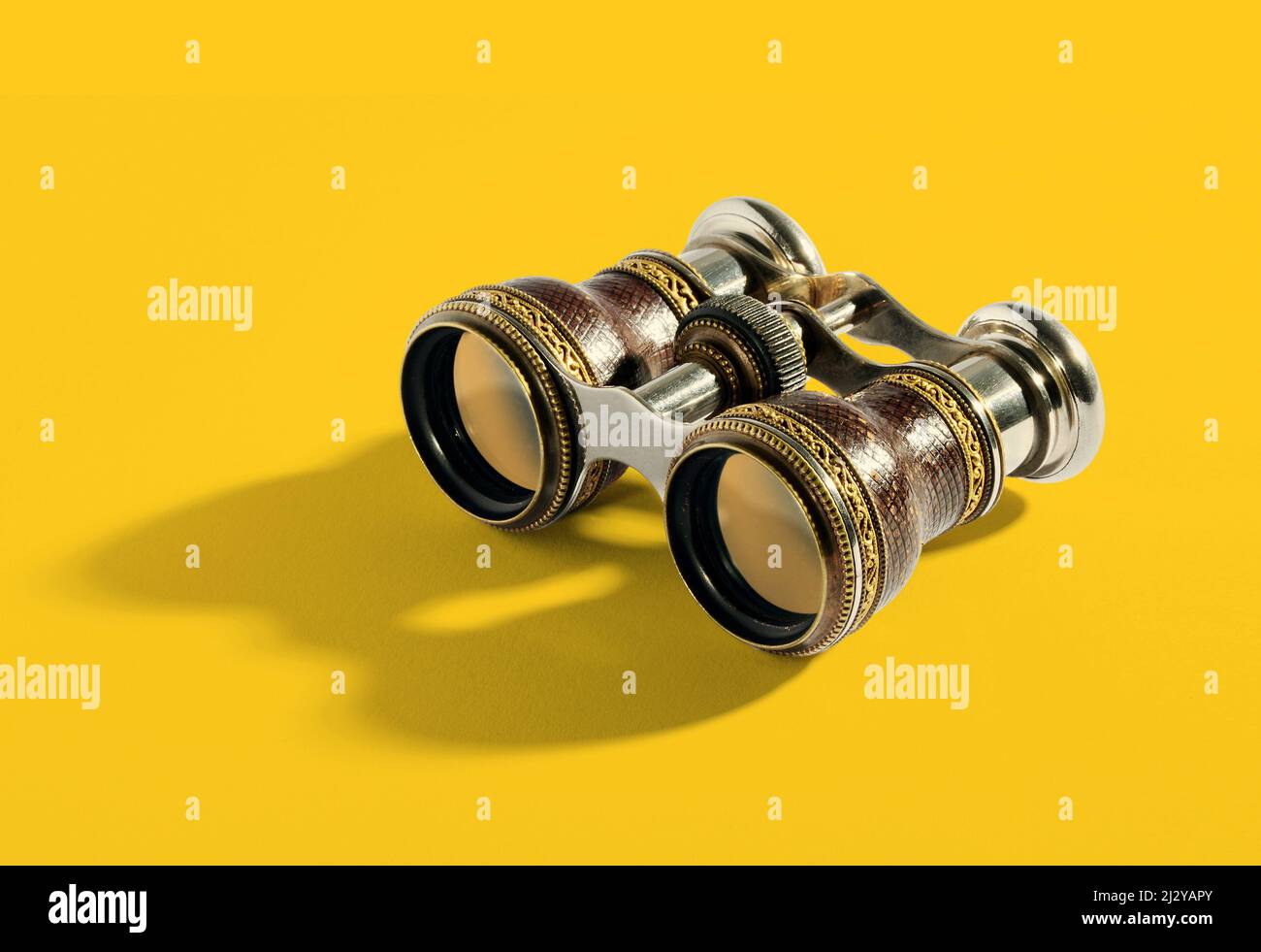 Pair of small vintage binoculars or opera glasses with a metal frame for magnifying objects at a distance on a yellow background with shadow detail Stock Photo