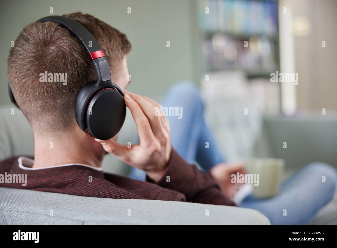 Close Up Of Man At Home Wearing Wireless Headphones Relaxing On Sofa Streaming Music OrListening To Podcast Stock Photo