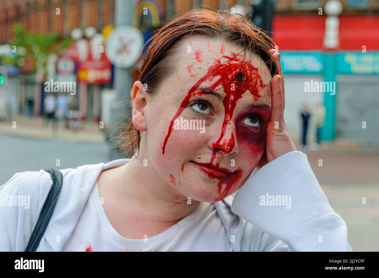 A young lady shows off her make up skills by fabricating a bullet wound on her forehead. Stock Photo