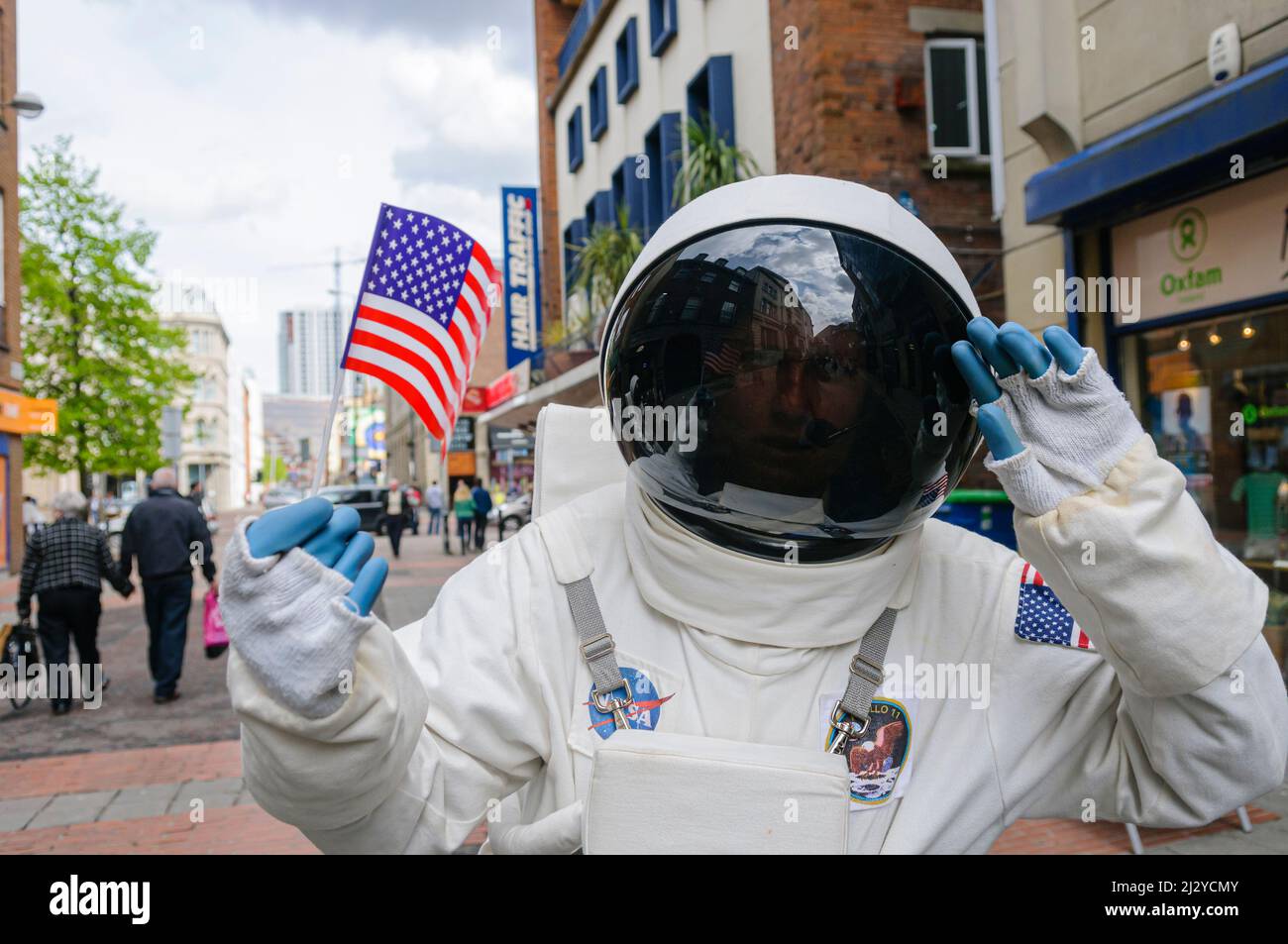 Person dressed as a NASA astronaut holding an American flag on a street during the annual Festival of Fools in Belfast Stock Photo