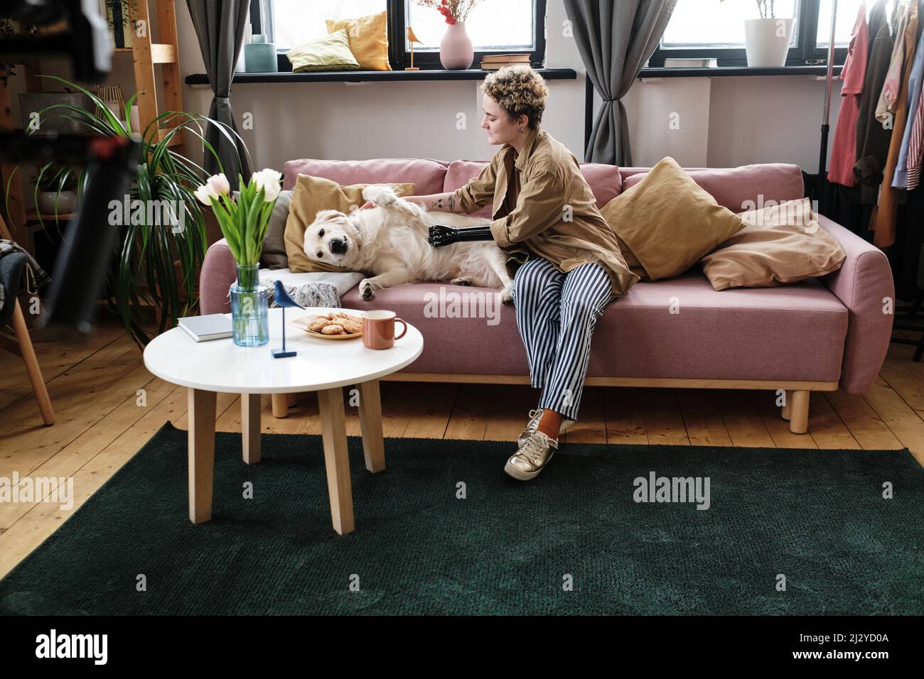 Girl having arm prosthesis petting her dog on sofa during leisure time