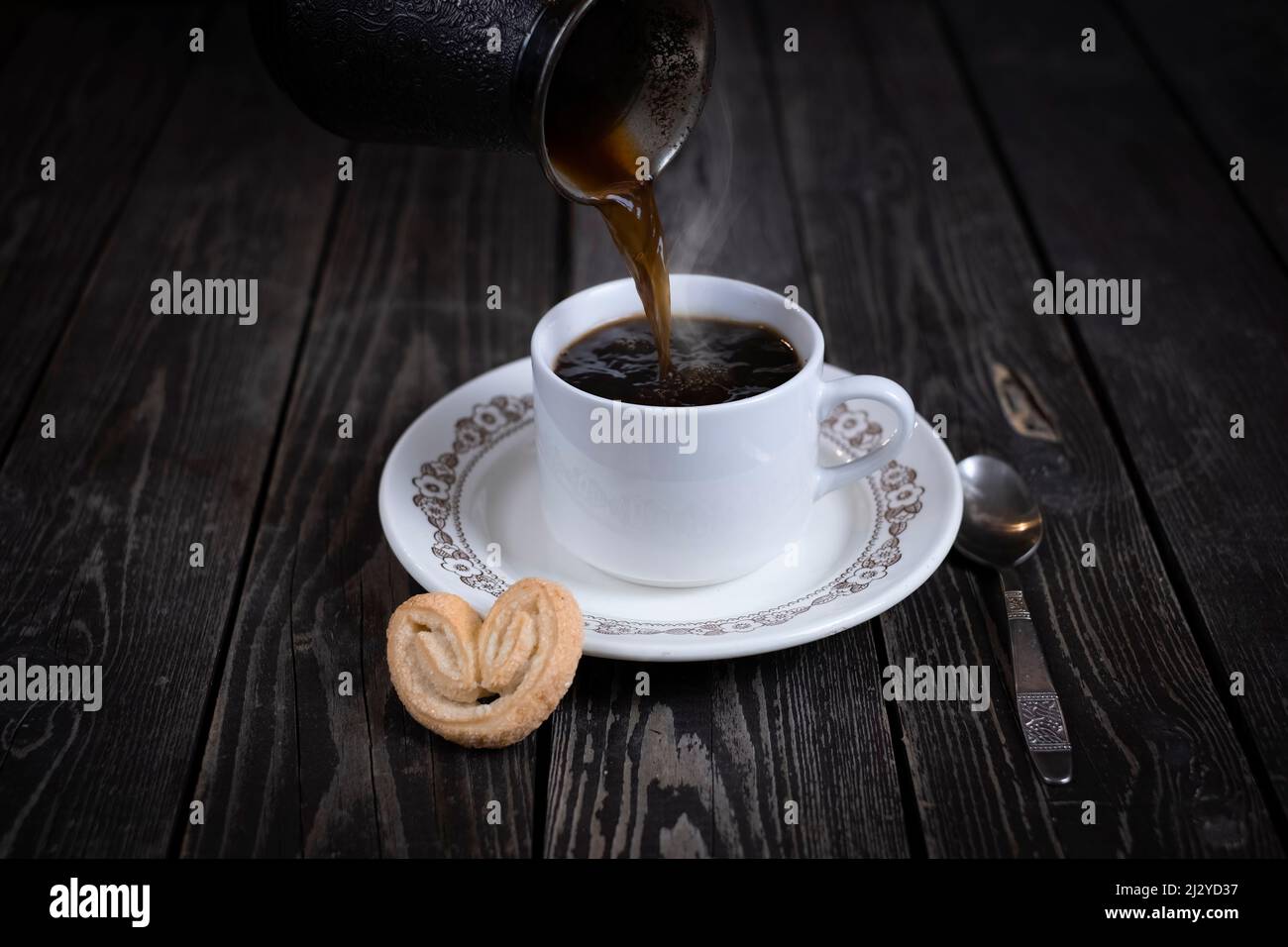 pouring black espresso coffee from coffee maker into white cup on wooden background Stock Photo