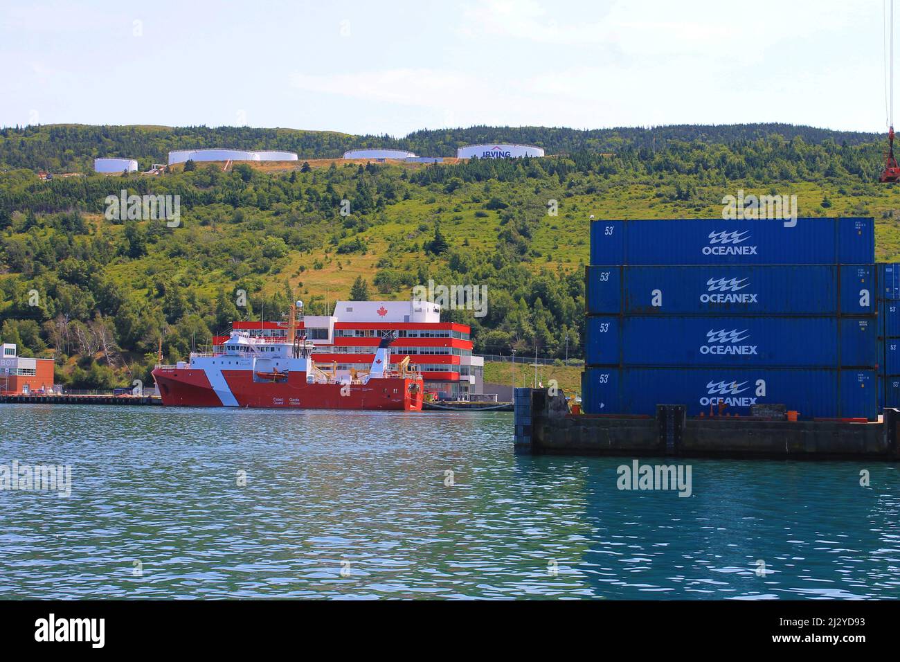 Shipping containers stacked on the end of a pier, Coastguard ship and building in background, St. John's Harbour. Stock Photo