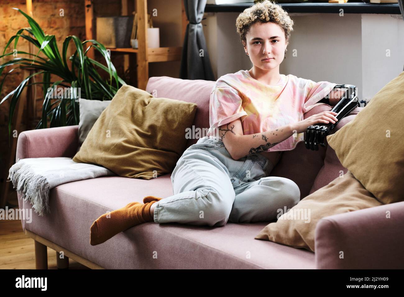 Portrait of young woman with prosthetic arm sitting on sofa in living room Stock Photo