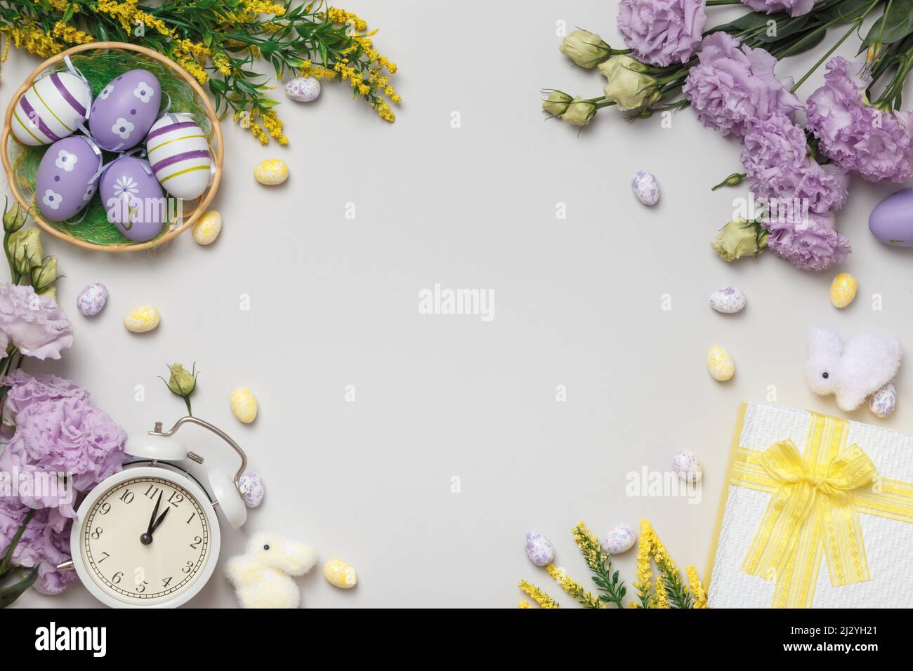 Easter concept on a gray background. Violet flowers and blooming yellow twigs gift eggs in a basket alarm clock. Stock Photo