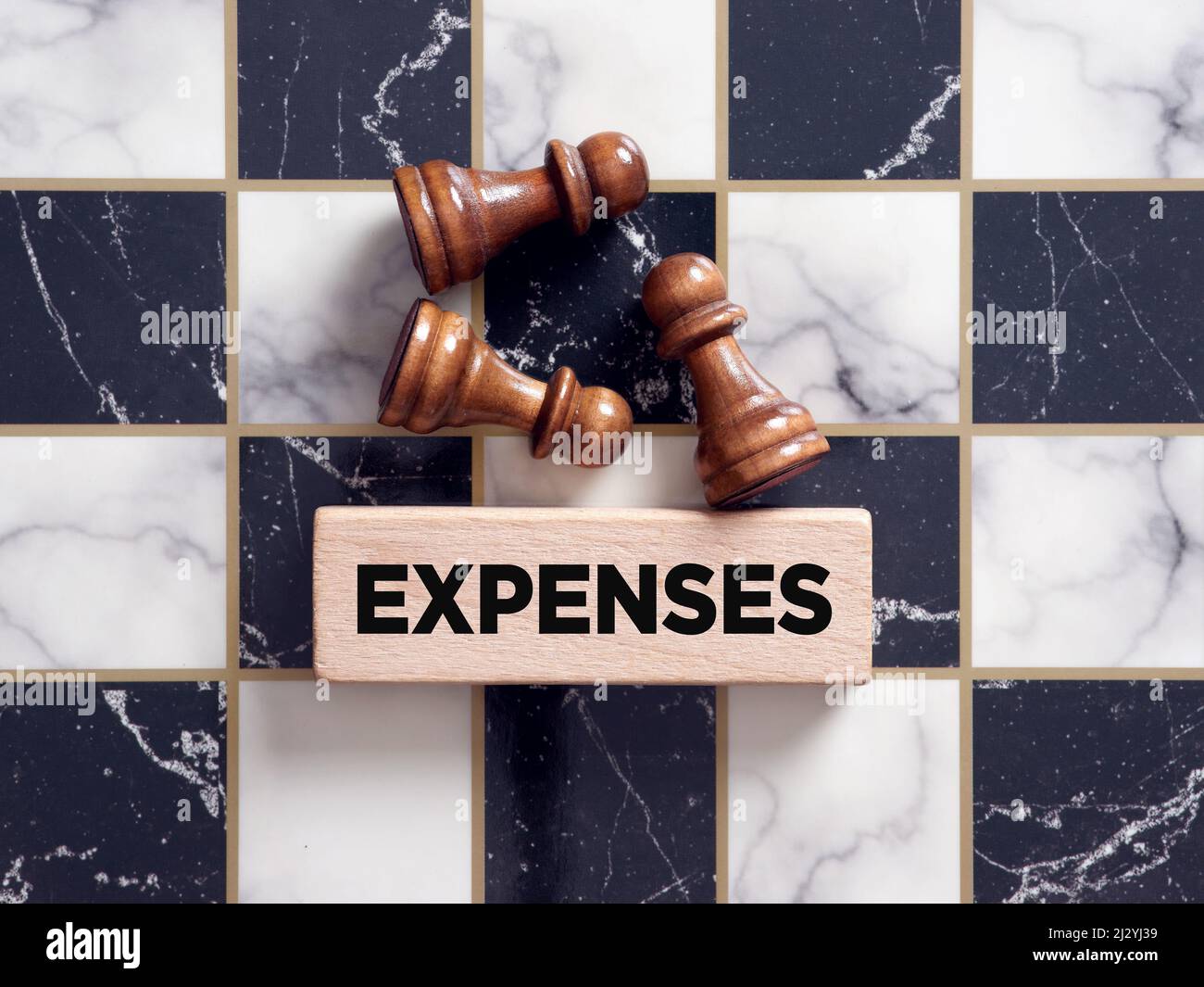 Chess piece pawns lying on the chessboard with the word expenses on a wooden block. Financial expenses and cost concept. Stock Photo