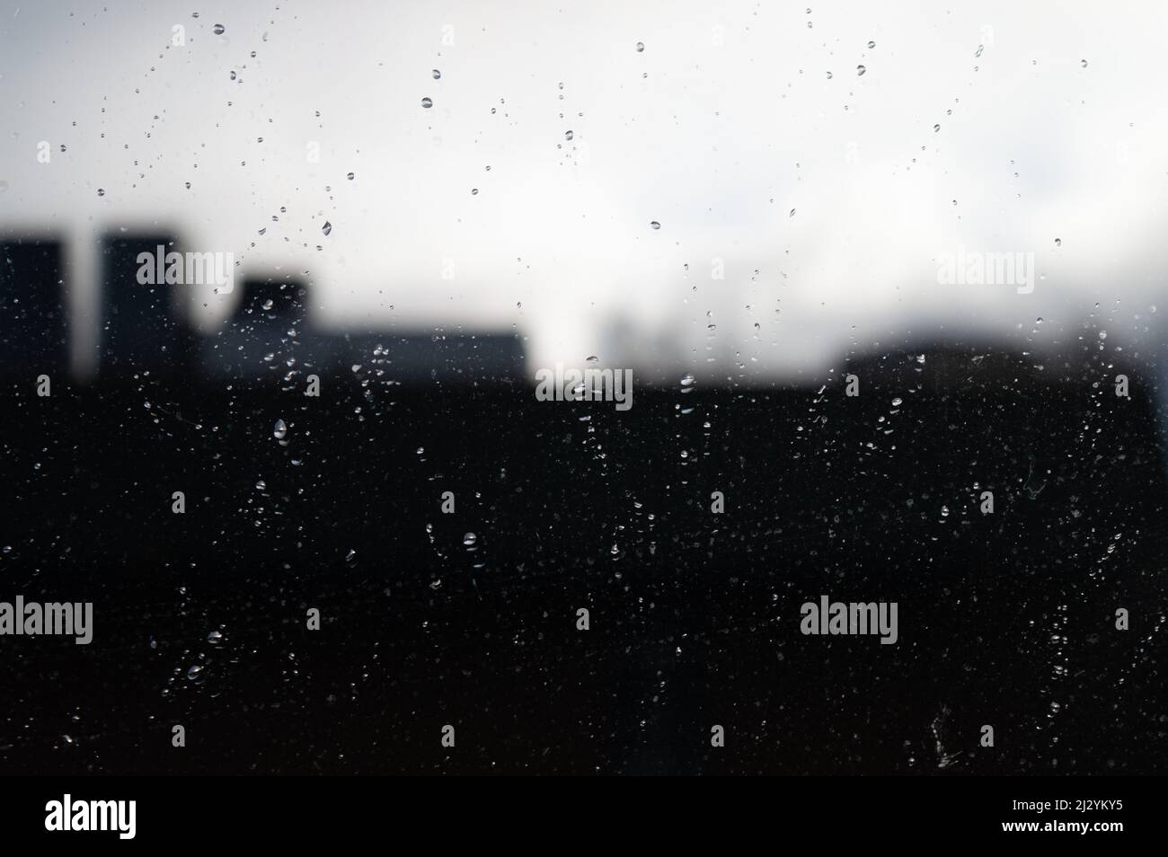 Blurred reflection of city silhouette in glass covered with raindrops Stock Photo