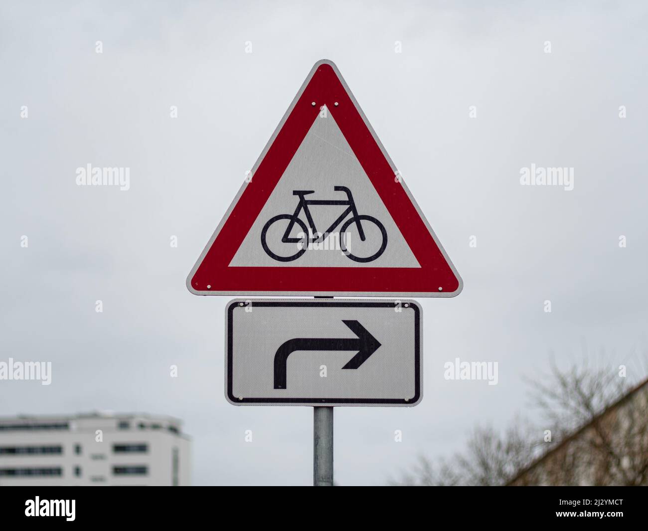Cyclists warning street sign with an arrow to the right. Road sign to pay attention to bicycle riders in a city. Symbol in front of an overcast sky. Stock Photo