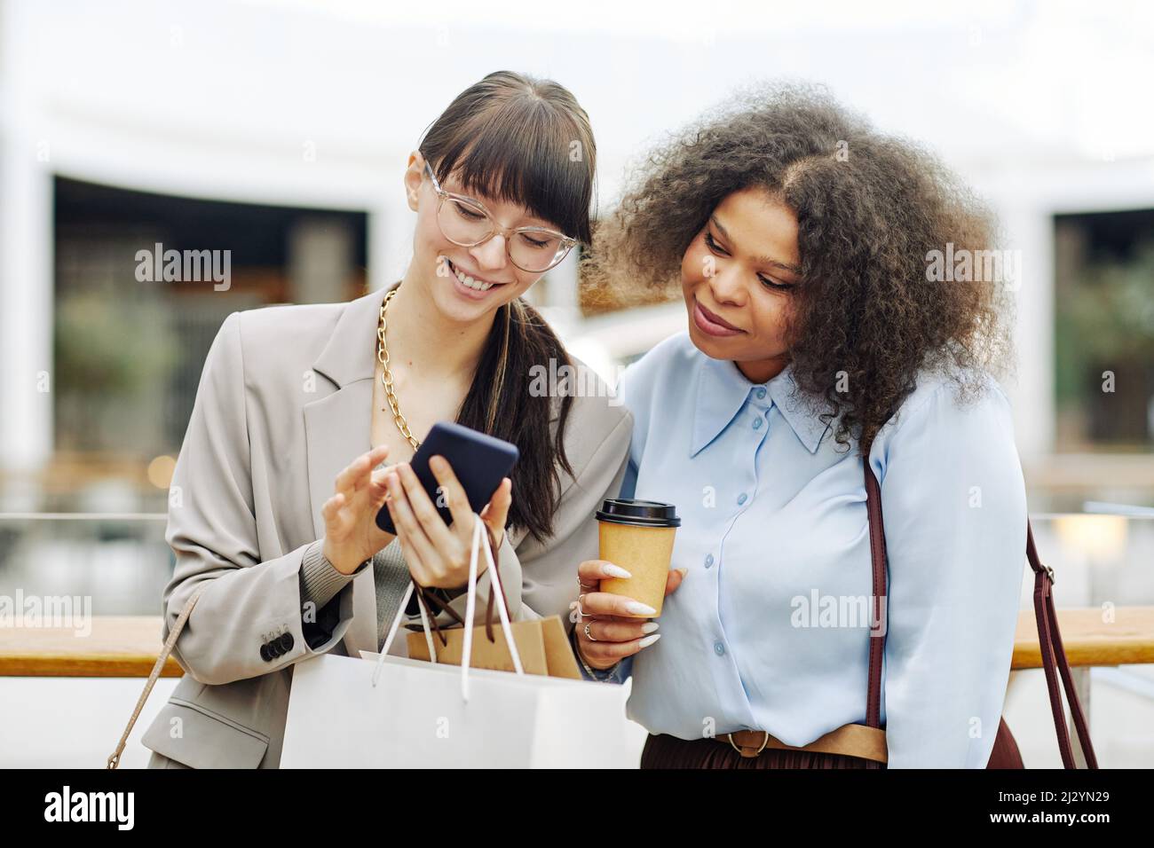 Waist up portrait of two smiling young women in shopping mall using ...