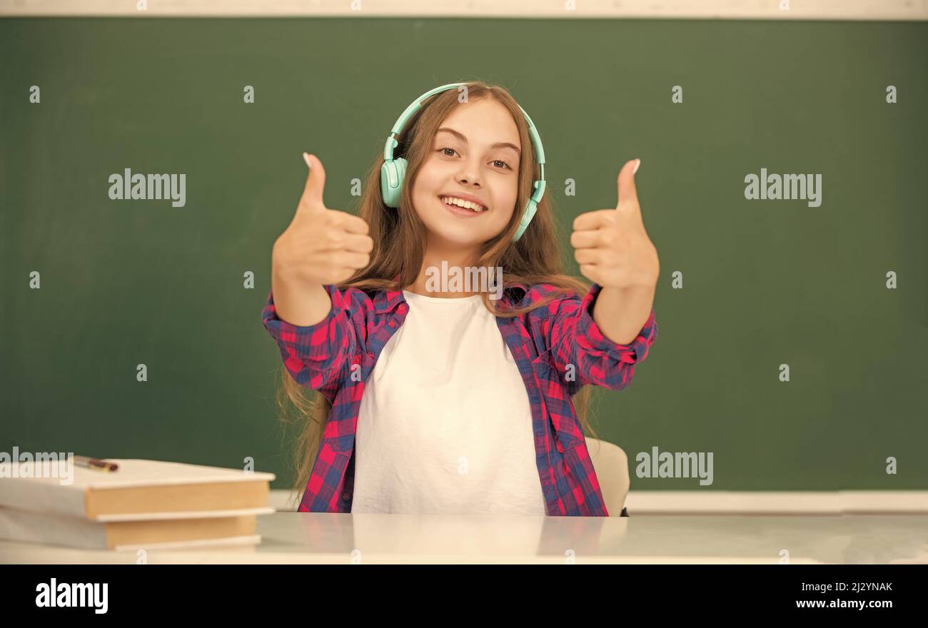 happy kid with earphones at blackboard showing thumb up, ebook Stock Photo