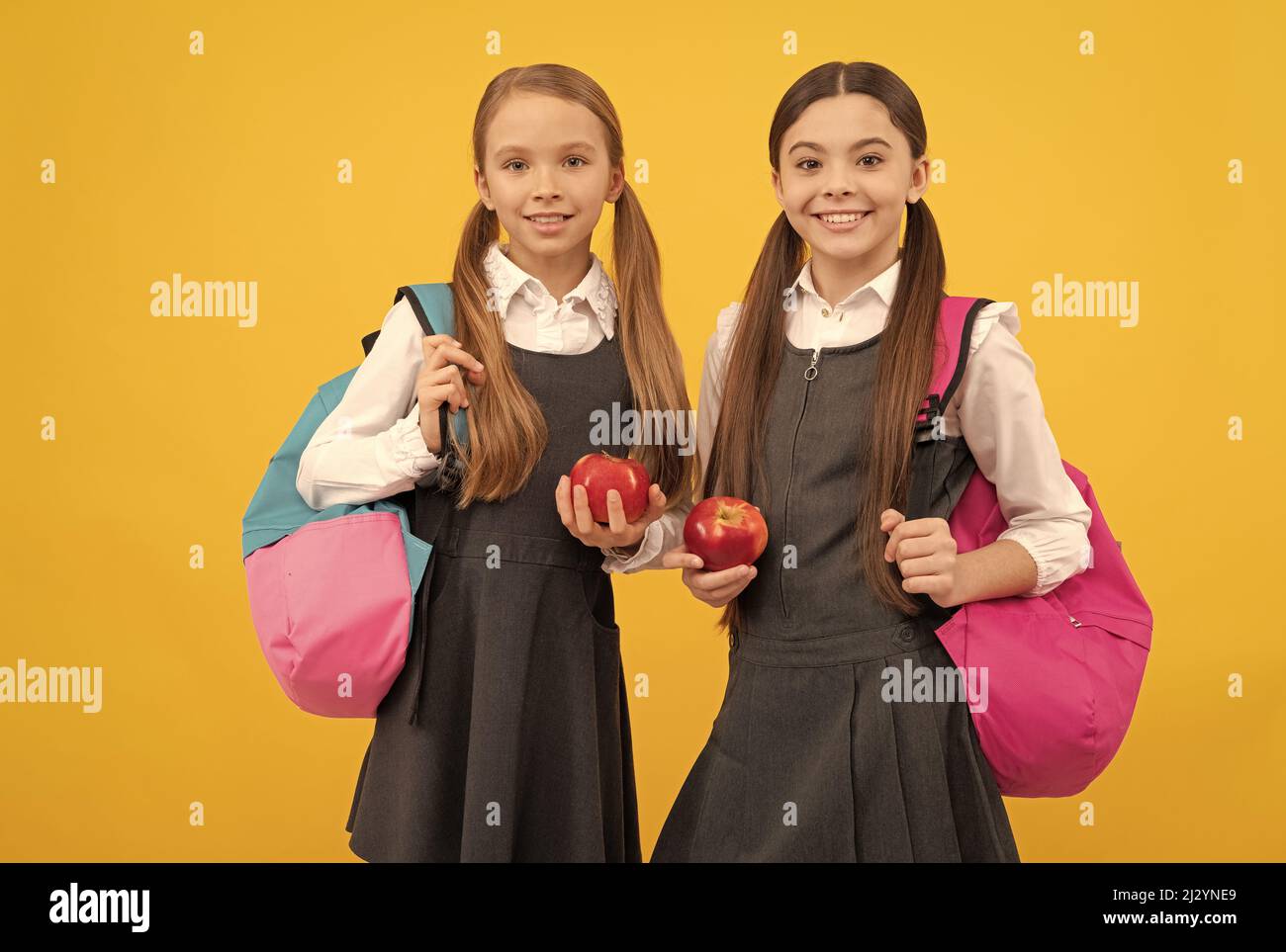 Hungry kids in formal uniforms hold vitamin apples for school snack yellow background, snacking Stock Photo