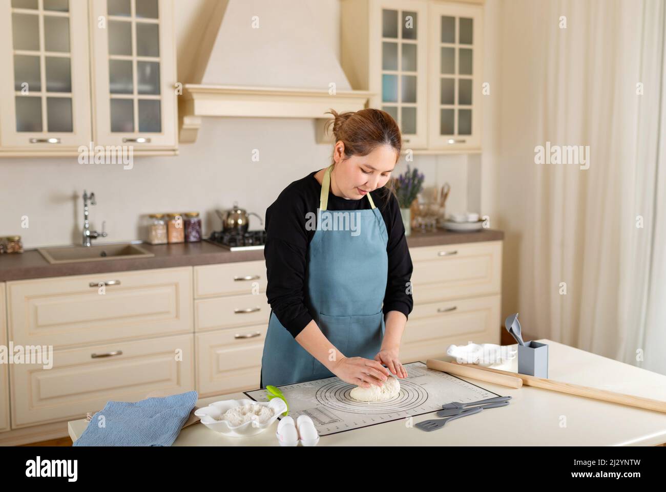 Young Central Asian woman cooking from dough in modern kitchen. Stock Photo