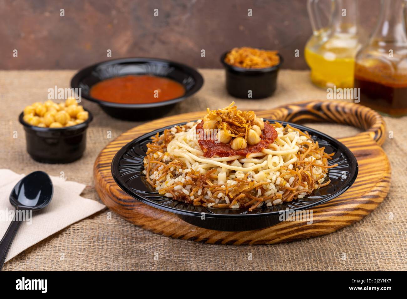 Transparent Plastic container with oriental honey sweets & cake with milk on a wooden table & black background, Black Plastic plate Stock Photo