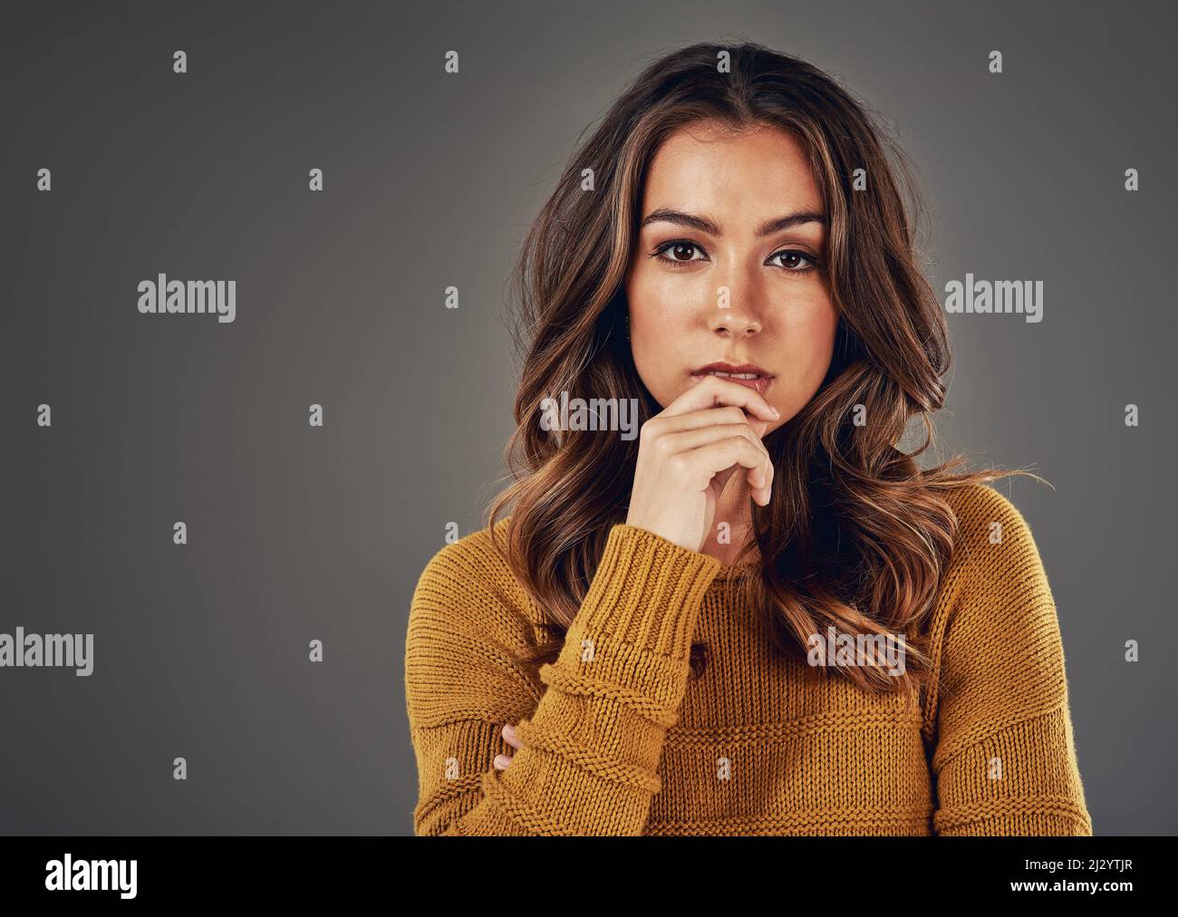 Pensive beauty. Studio portrait of an attractive young woman posing against a grey background. Stock Photo