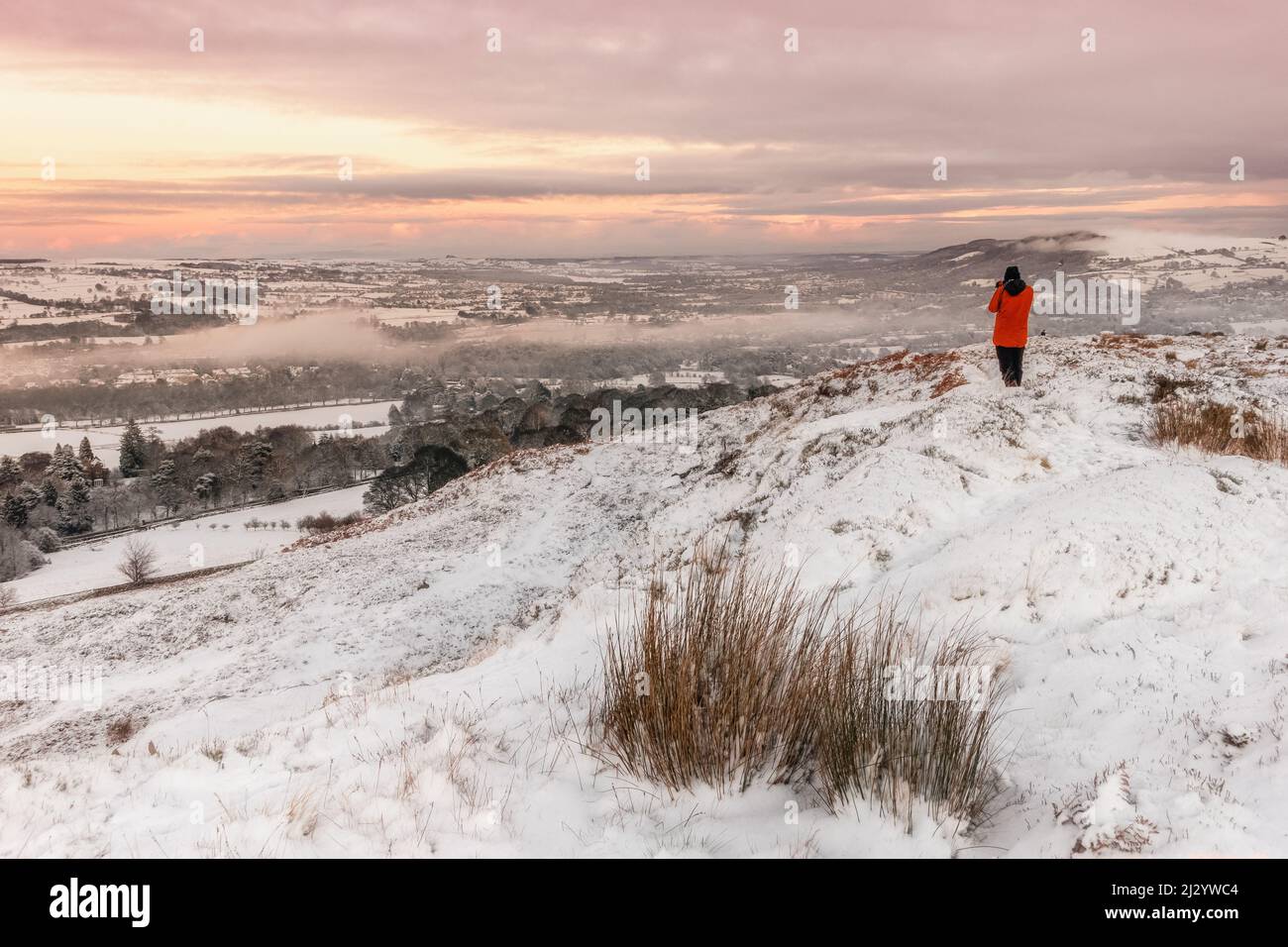 Photographer taking photos of sunset on a snowy day on Burley Moor overlooking Burley-in-Wharfedale, West Yorkshire, England, UK Stock Photo