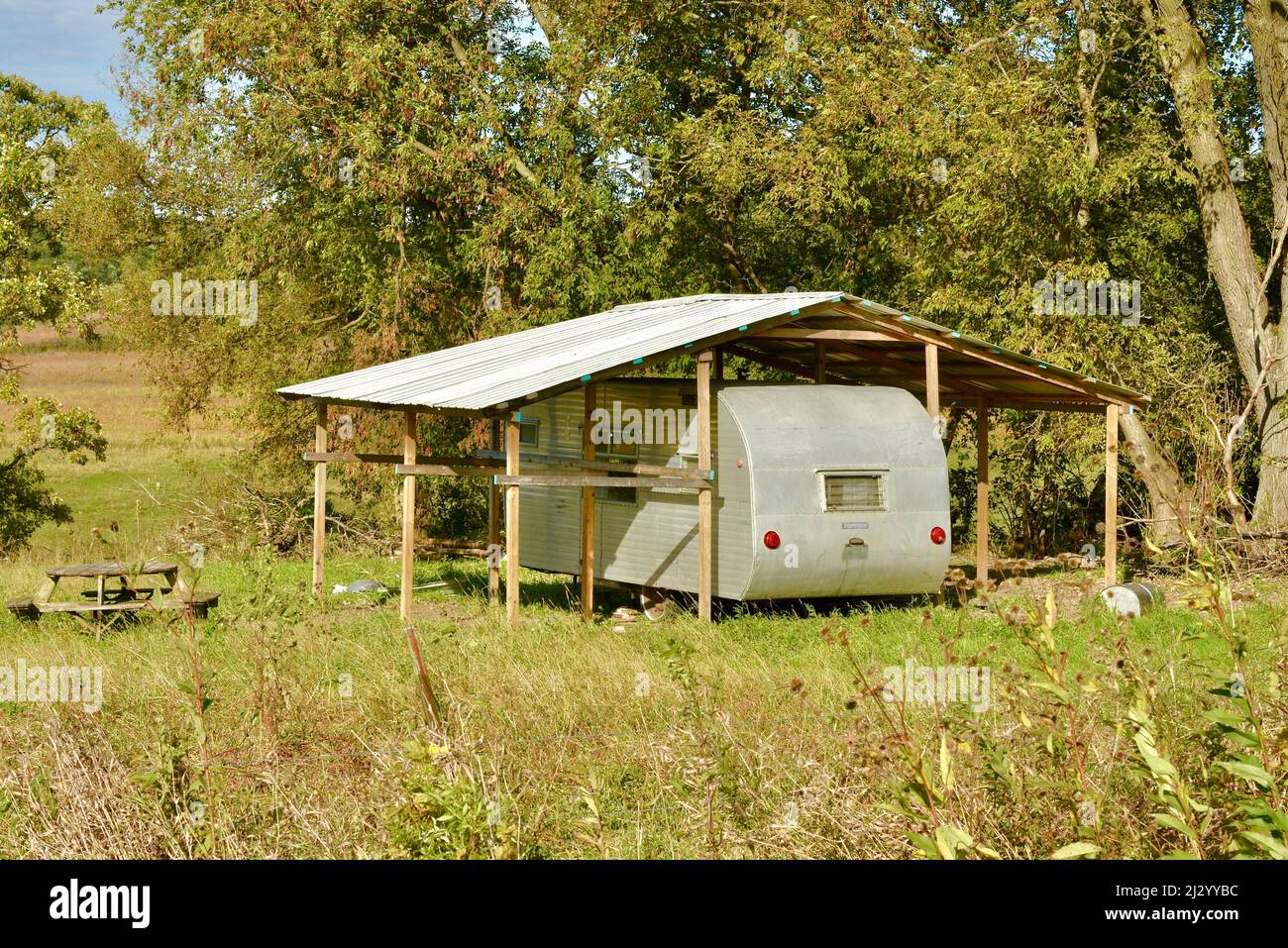 Trendy, hip, silver metal vintage camper trailer parked under protective metal roof at remote