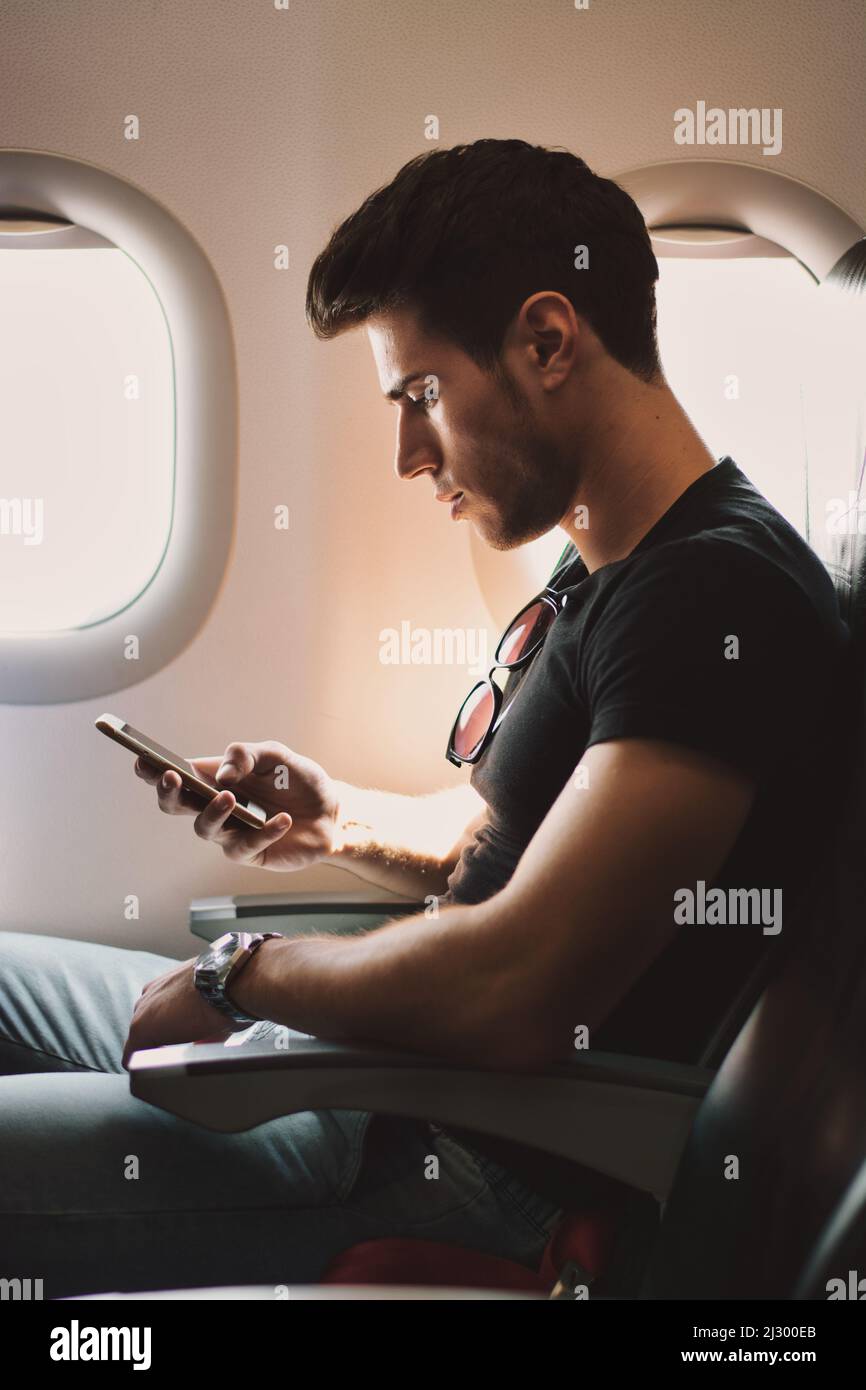 Young man against plane window using cell phone Stock Photo
