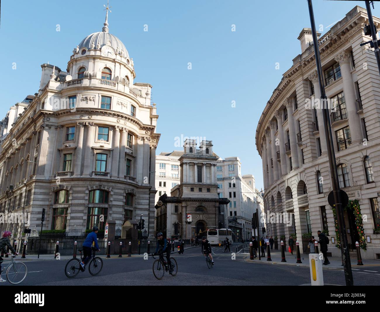 Cyclists at a crossroads or intersection with Bank tube station behind and various buildings either side, London. Stock Photo