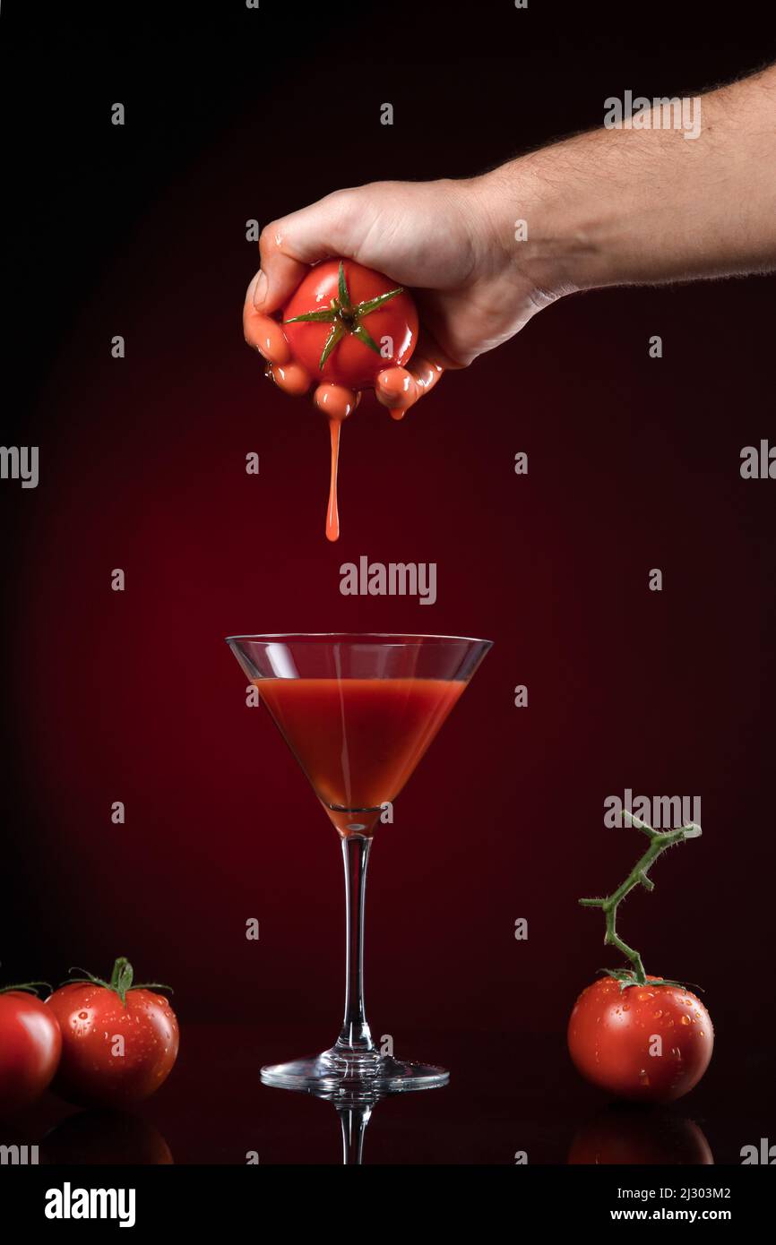 Hand picking a tomato from a tomato juice on dark red background. Stock Photo