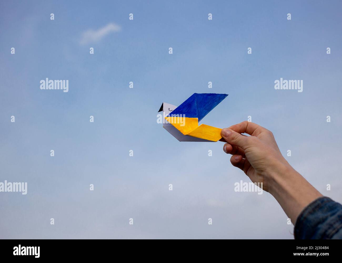 paper dove of peace in his hand, wings are painted in yellow and blue colors of the Ukrainian flag against sky. A symbol of peace. Support Ukraine. St Stock Photo