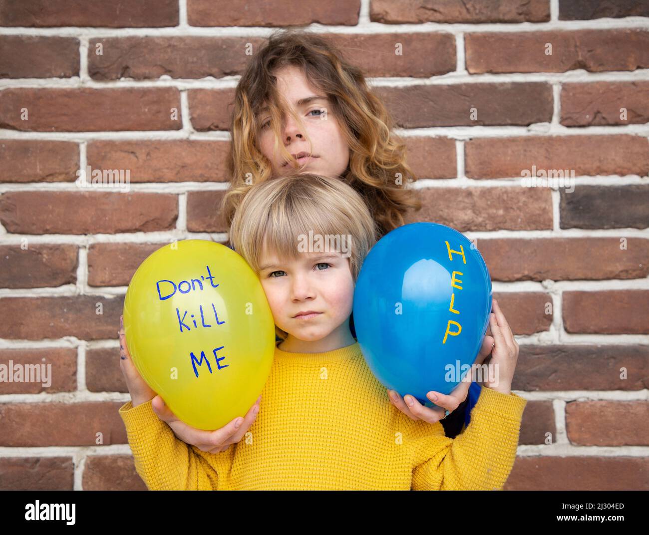little boy and adult girl with blue and yellow balloons with inscriptions dont kill me and help. Children against war. stand with Ukraine. Fear, drawi Stock Photo