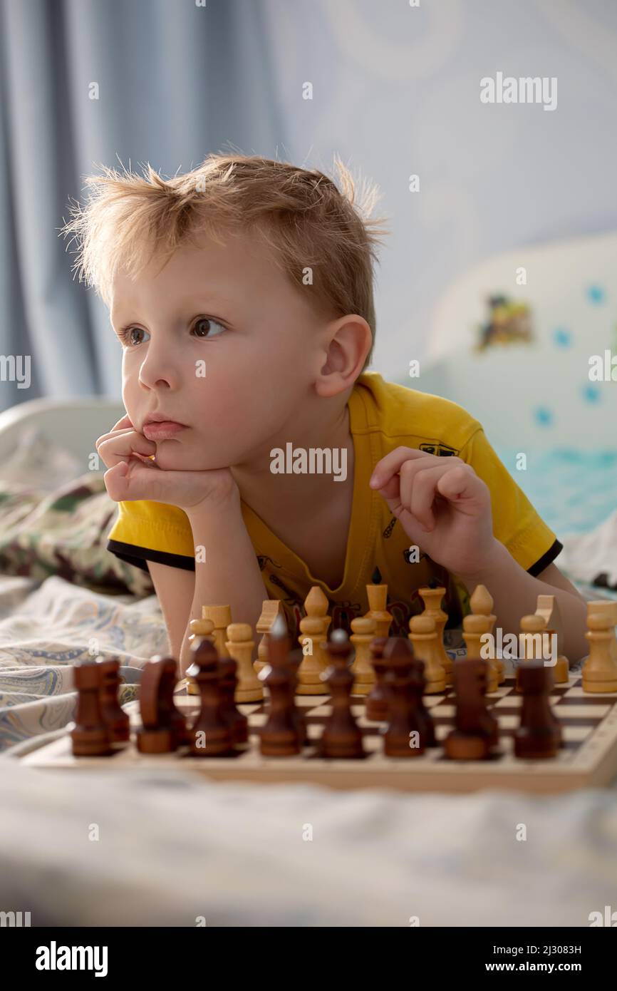 A little boy, lying on the bed in front of a chess board, is playing chess with his dad Stock Photo