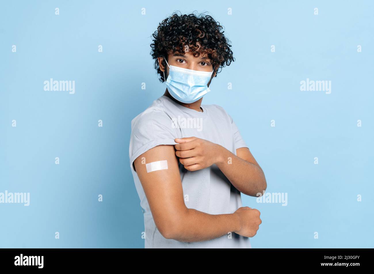 Indian or Arabian man with medical protective mask in face and with a band-aid on shoulder, received a vaccine, protection against covid 19, and oIndian or Arabian man with medical protective mask in Stock Photo