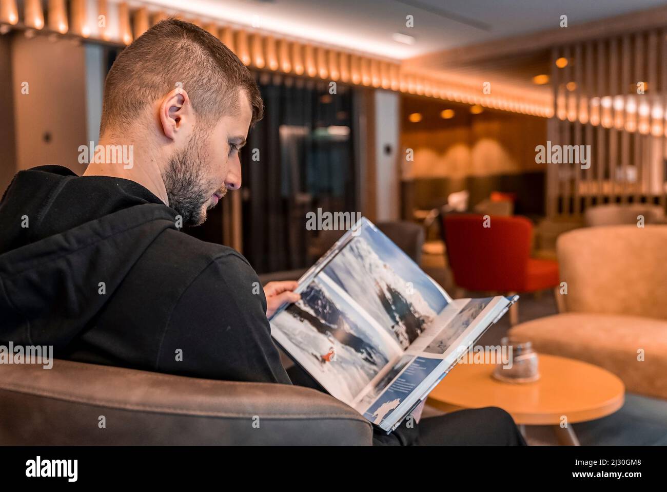 Man reading travel catalog while sitting on armchair in hotel lobby Stock Photo