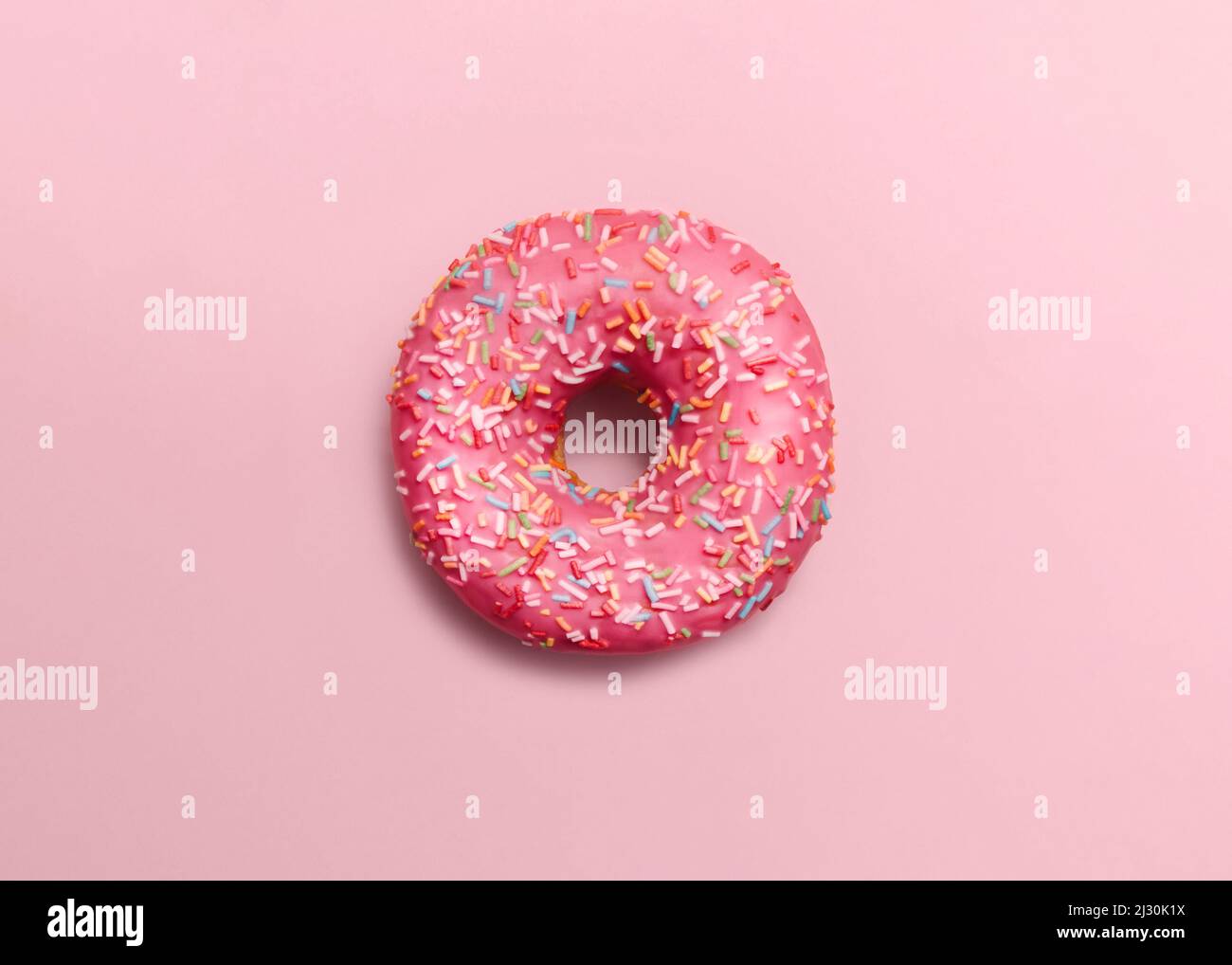 Pink glazed doughnut with sprinkles on pastel pink backdrop Stock Photo
