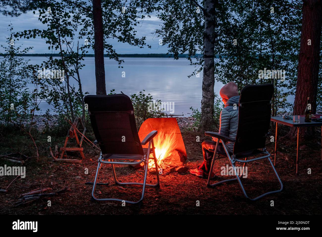 Woman sitting by the campfire in the forest on the banks of Lake Siljan in Dalarna, Sweden Stock Photo