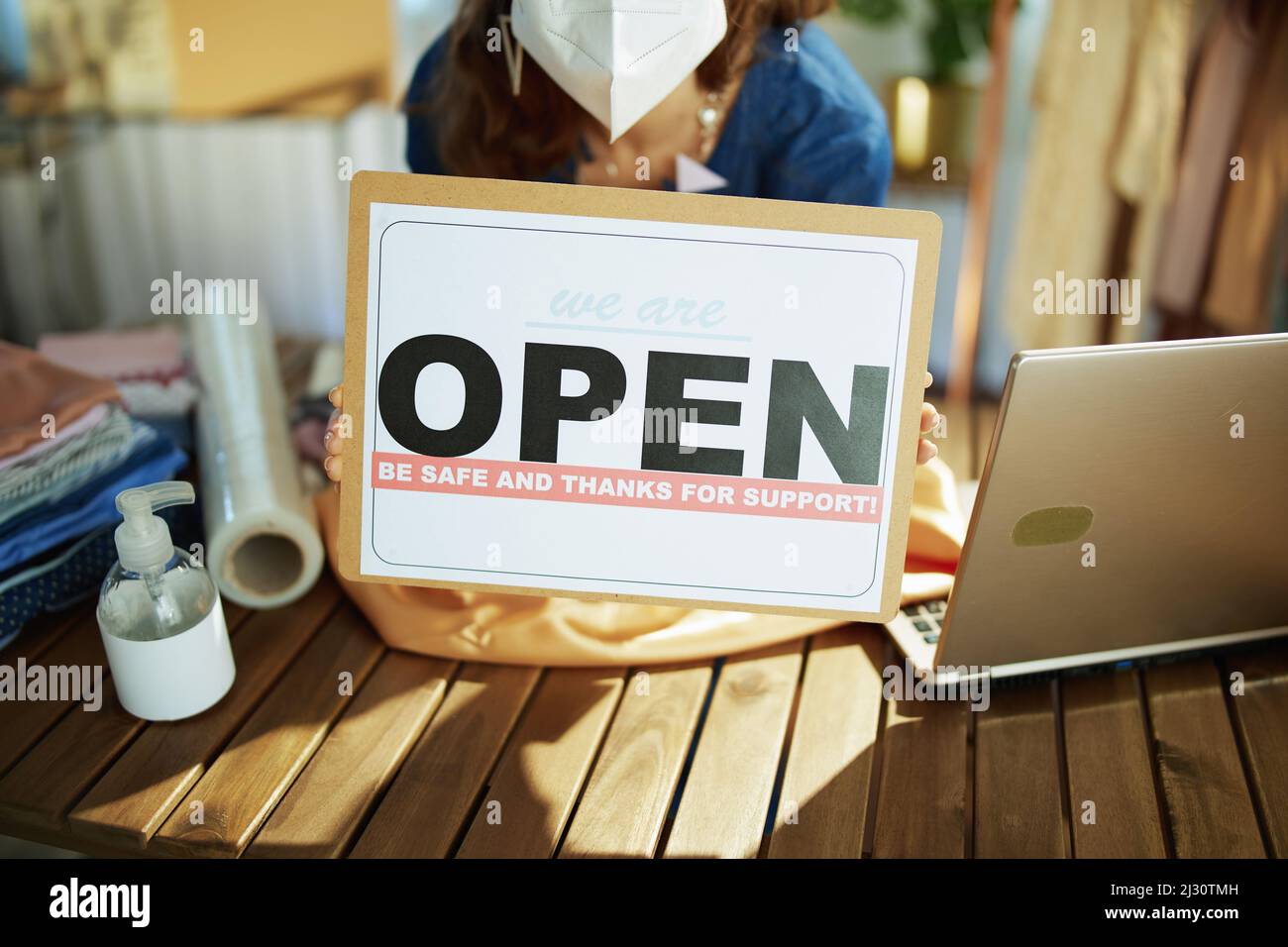 Closeup on small business owner woman with ffp2 mask, open after covid sign and disinfectant in the office. Stock Photo