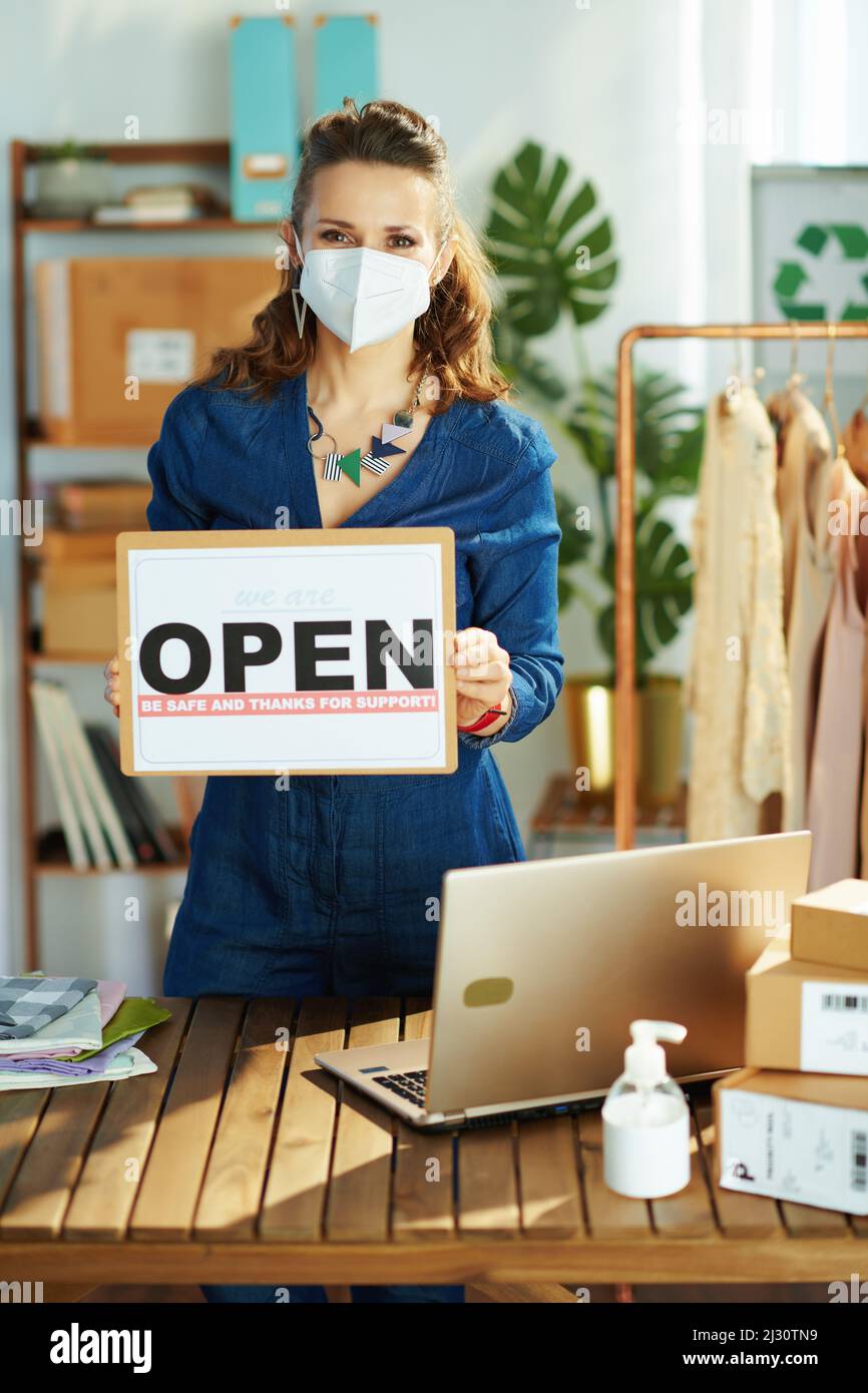 modern 40 years old small business owner woman with ffp2 mask, open after covid sign and sanitiser in the office. Stock Photo