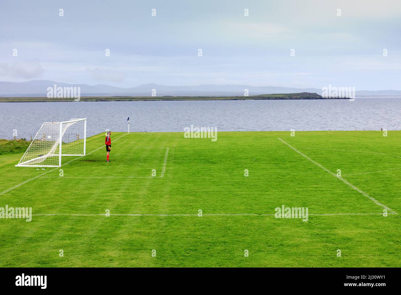 Lone goalkeeper, rural soccer field in front of the sea, Port Charlotte, Islay, Inner Hebrides, Scotland UK Stock Photo