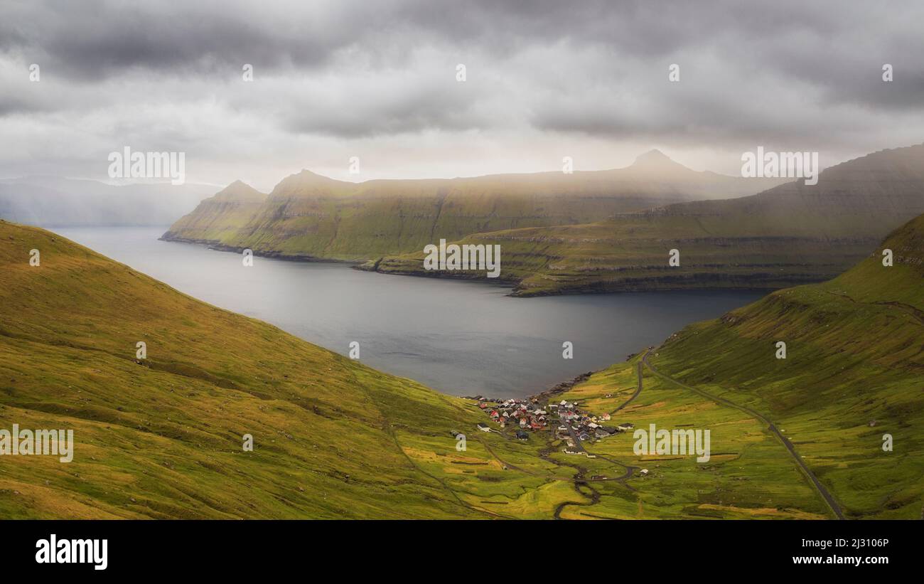 View of a lonely village in a wide landscape. Funnings, Eysturoy, Faeroer. Dark clouds, glimmers of light Stock Photo