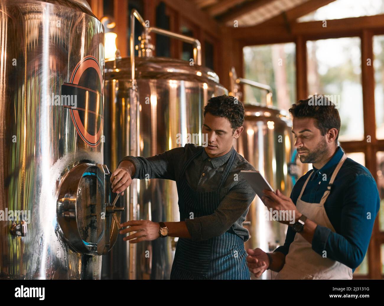 Lets hope this batch is a good one. Shot of two young working men doing inspection of their beer making machinery inside of a beer brewery during the Stock Photo