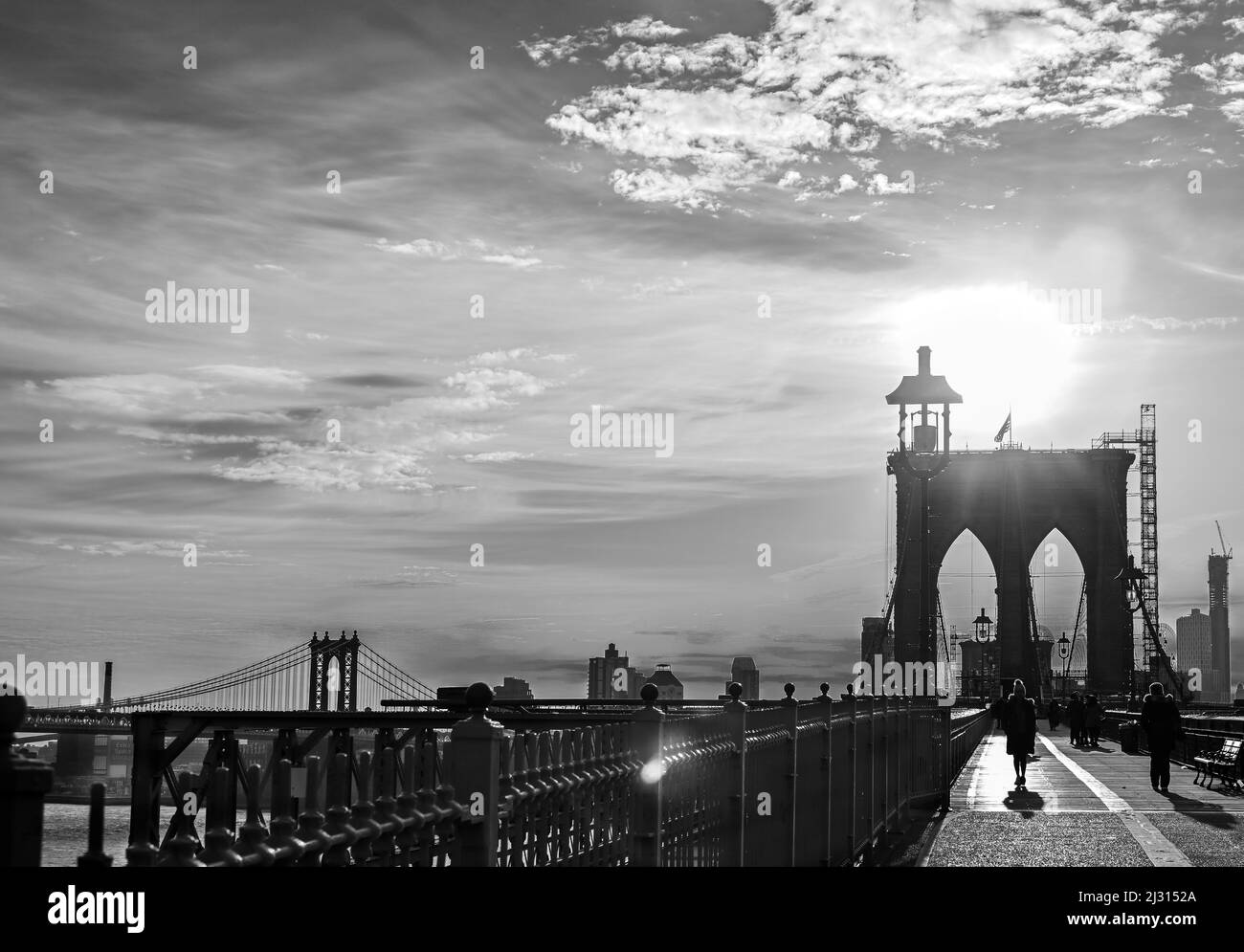 sihouettte of a woman in a coat walking across the Brooklyn Bridge in the early morning light Stock Photo