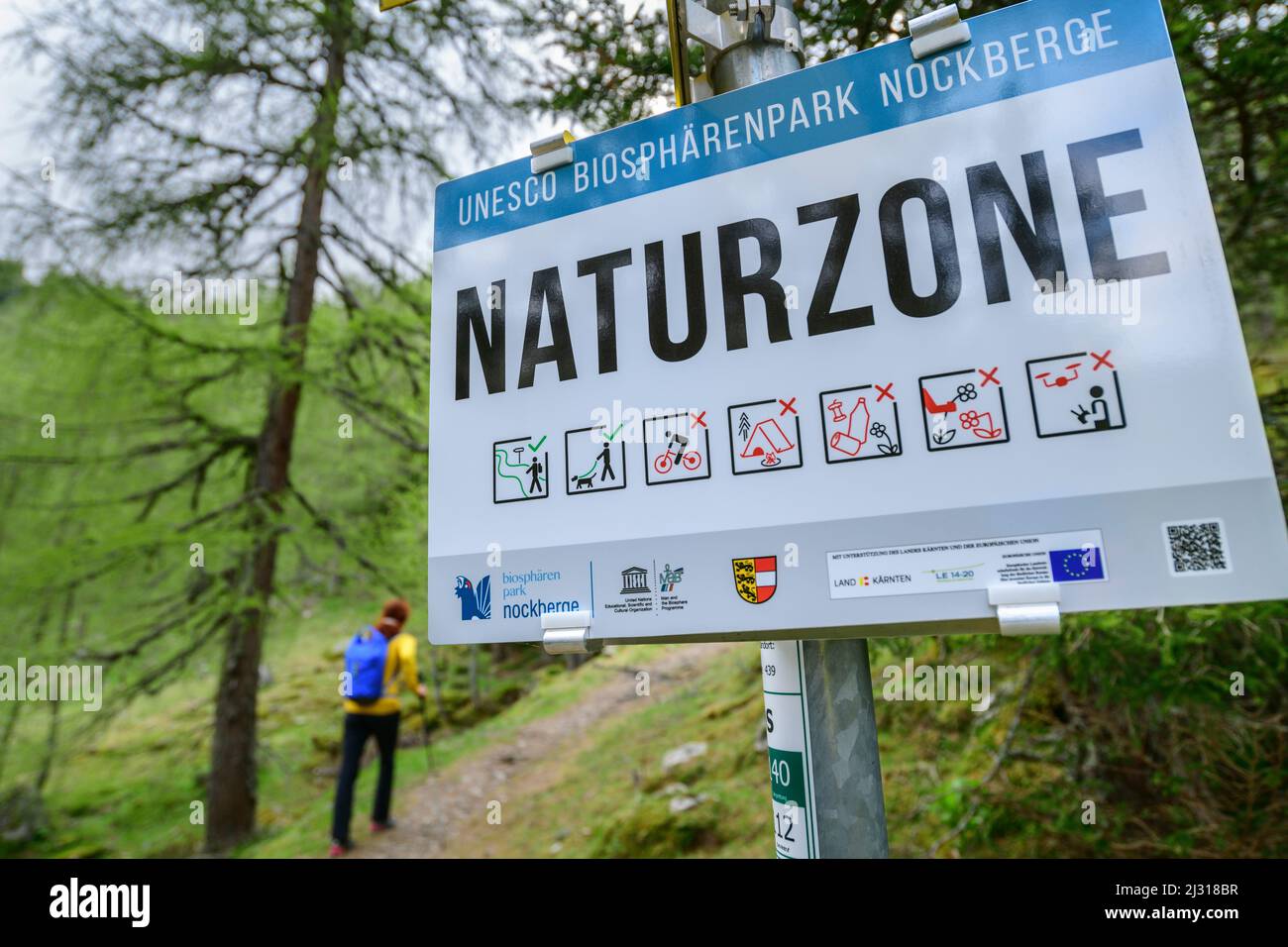 Sign nature zone with woman hiking out of focus in the background, Nockberge, Nockberge-Trail, UNESCO Nockberge Biosphere Park, Gurktal Alps, Carinthia, Austria Stock Photo