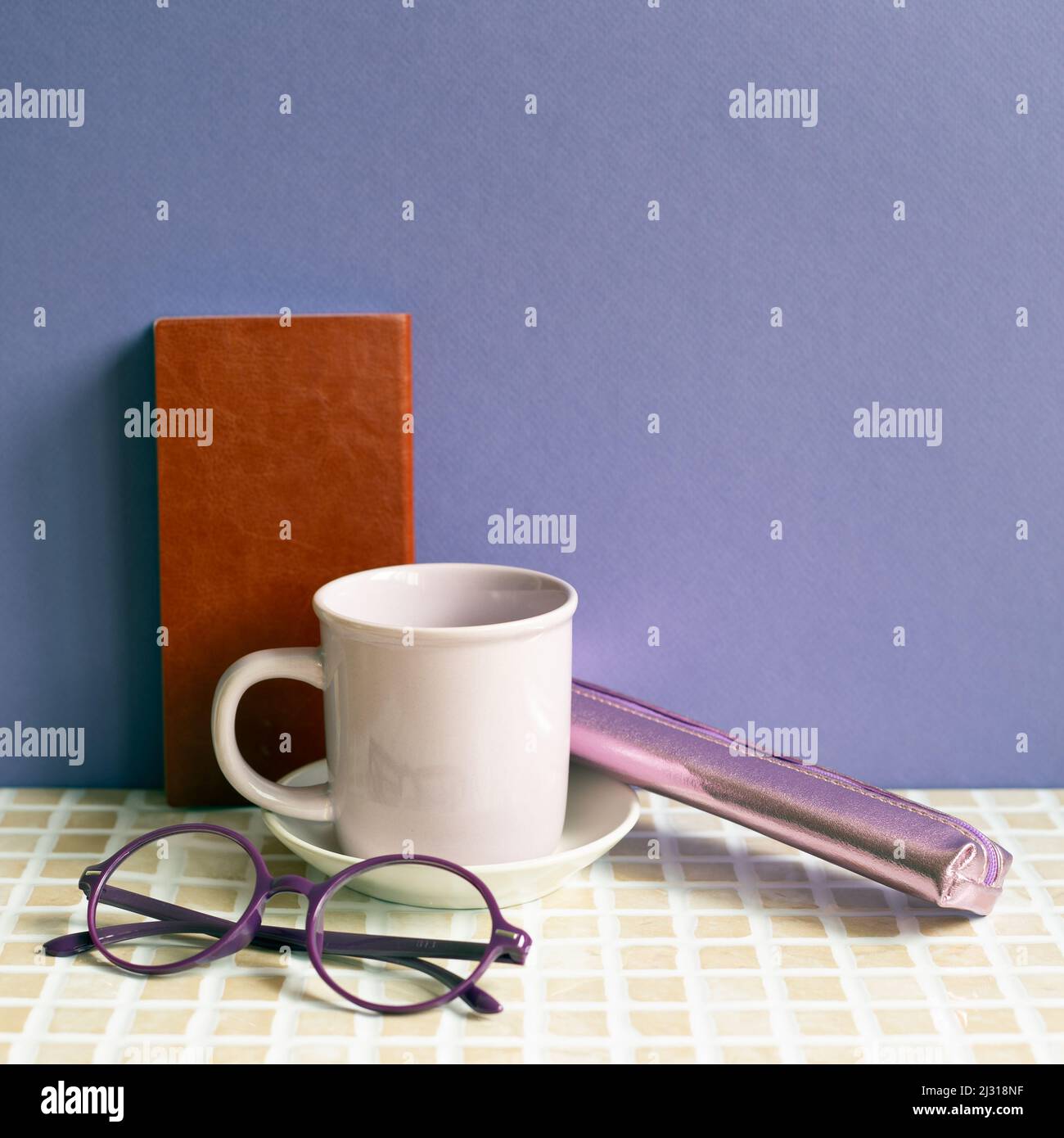 Notebook and coffee cup, glasses, pencil case on desk. purple wall background. workspace Stock Photo