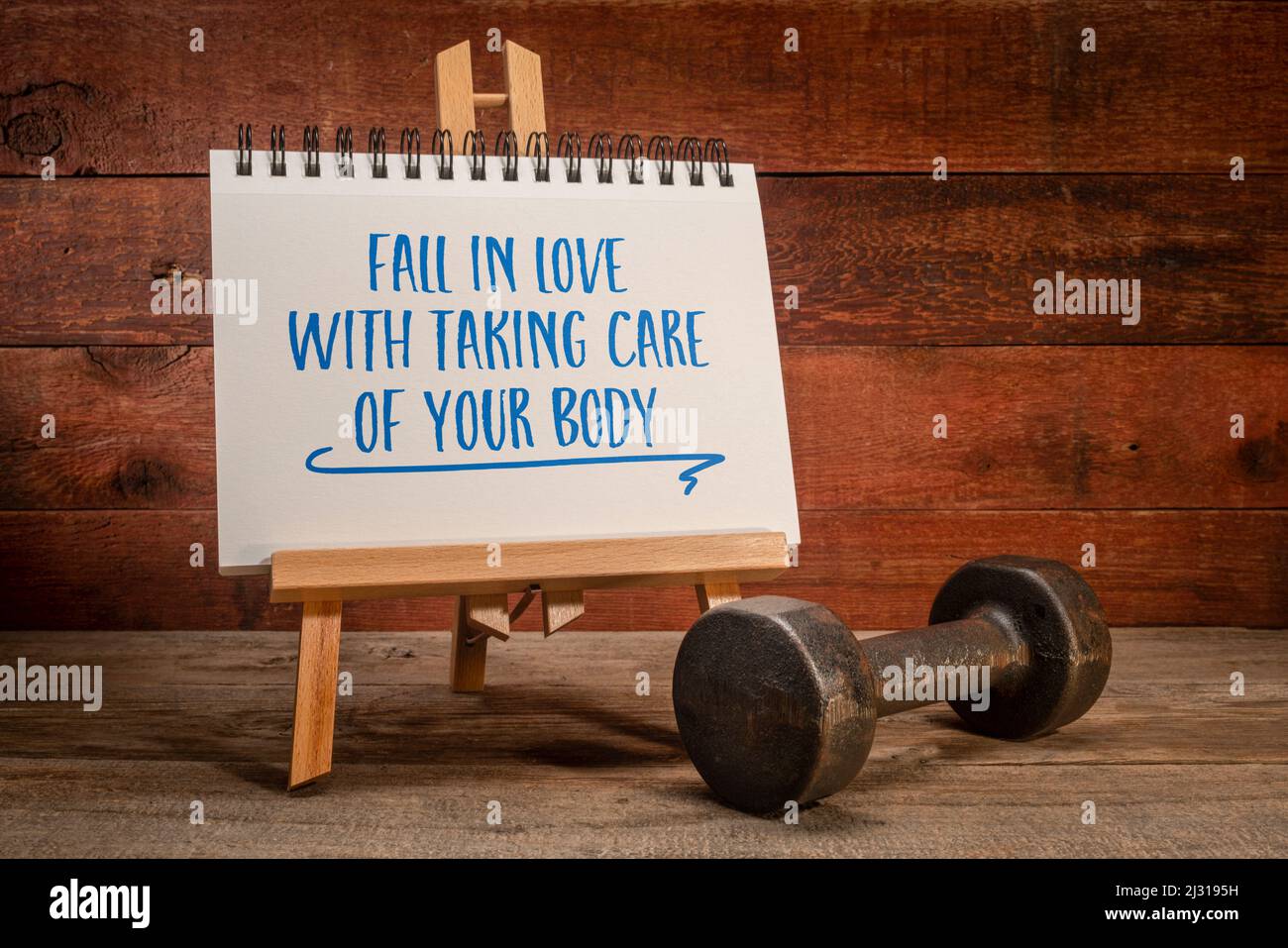 fall in love with taking care of your body, exercise and self care concept, small easel sign with a dumbbell against rustic wood Stock Photo