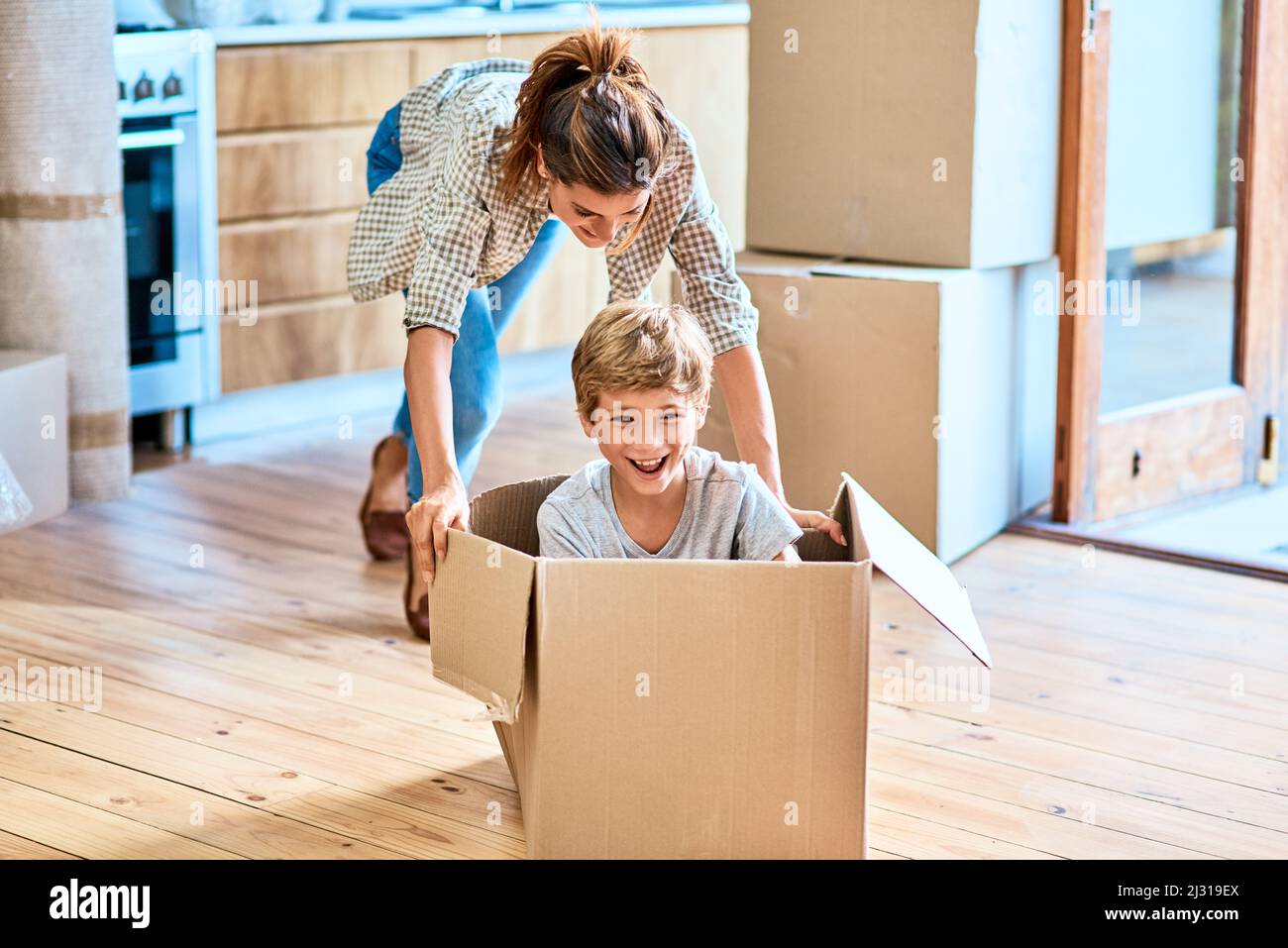 We have liftoff. Shot of a cheerful young woman pushing her son around in a box imagining its a car inside at home during the day. Stock Photo