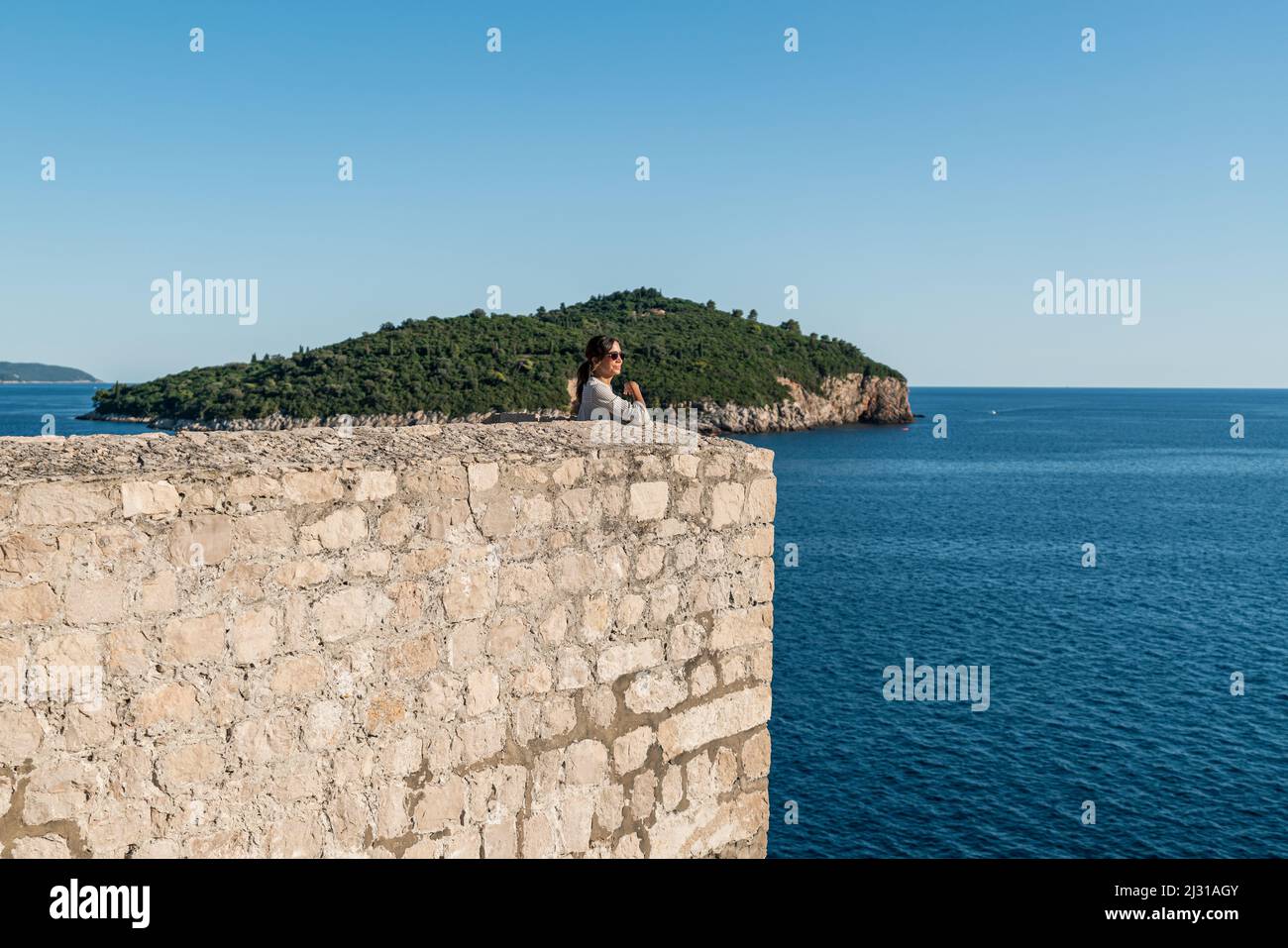 Woman looks out to sea from the city walls of the old town in Dubrovnik, Dalmatia, Croatia. Stock Photo
