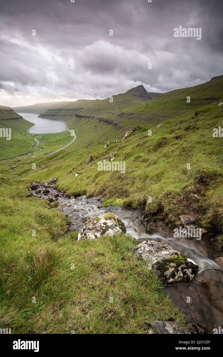 View of fjord and strait, Streymoy, Faeror Islands, dark clouds, watercourse in foreground Stock Photo